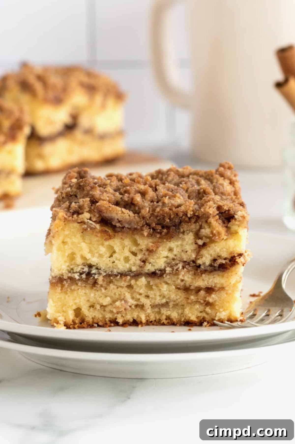 A square slice of classic coffee cake on a stack of white ceramic plates with a metal fork, showcasing the distinct layers.
