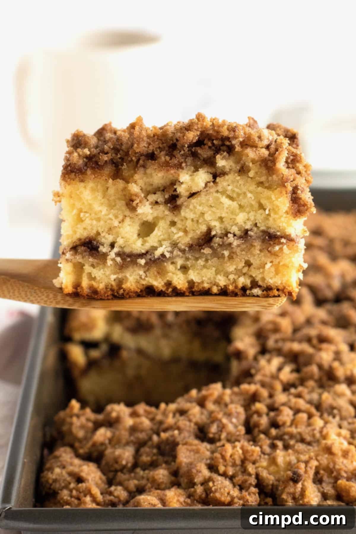 A slice of classic coffee cake being lifted from the pan on a wooden spatula, showing its layers.