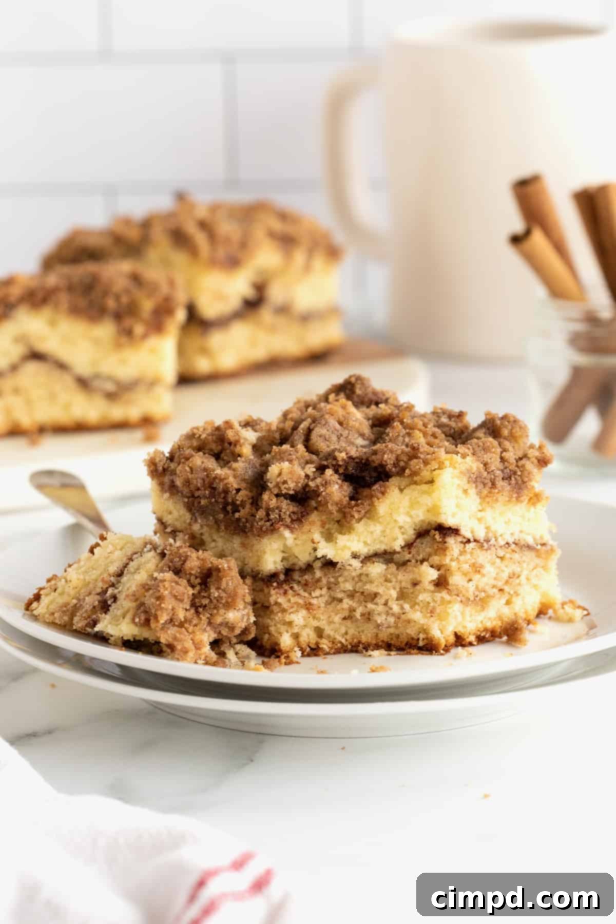 A square slice of classic coffee cake on a stack of white ceramic plates with a metal fork.