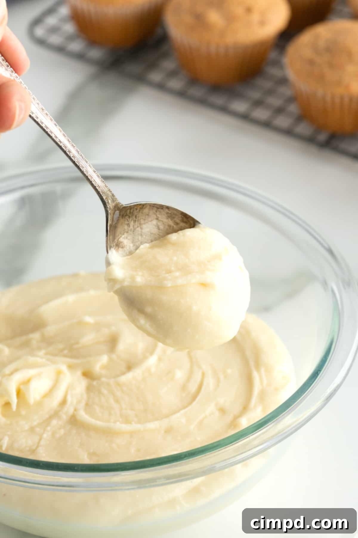 Whip Up Perfect Cream Cheese Frosting 3 A spoon full of cream cheese frosting over a glass bowl.
