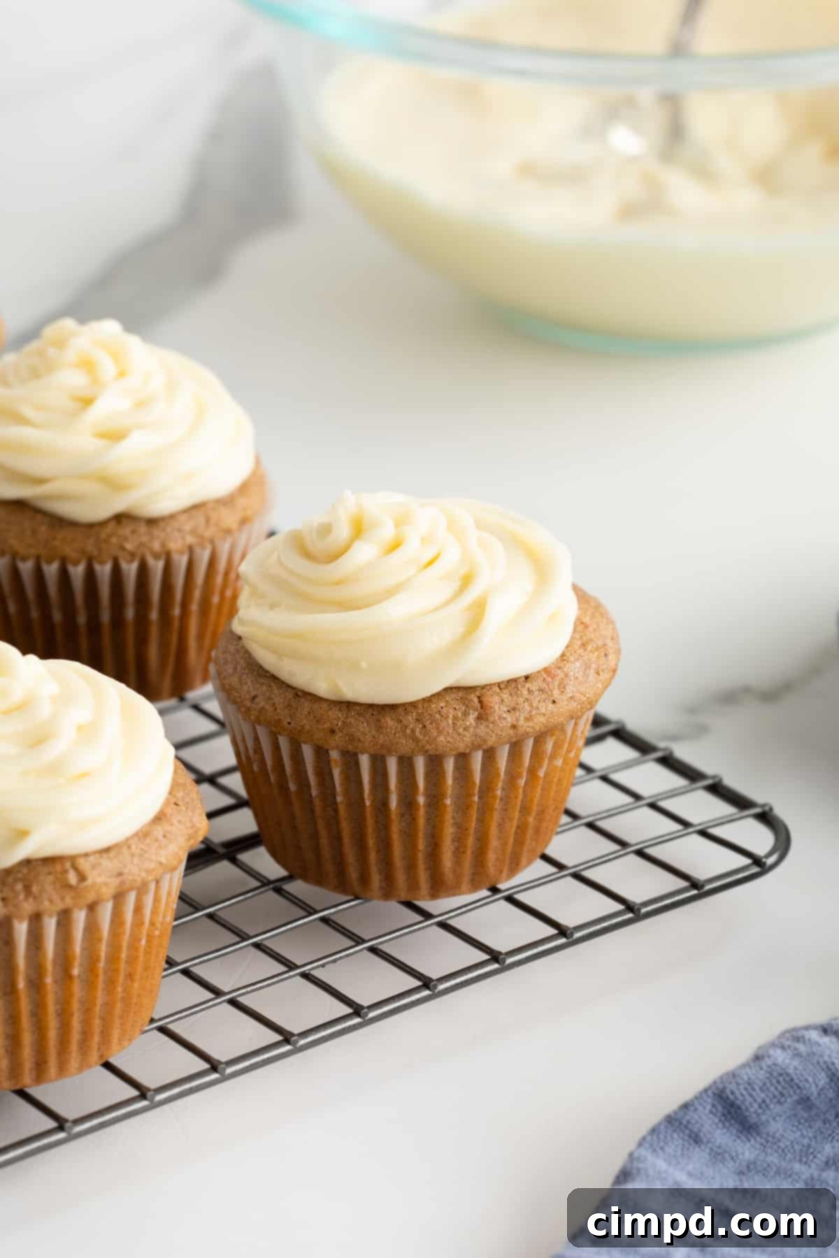 Whip Up Perfect Cream Cheese Frosting 7 Three vanilla cupcakes with cream cheese frosting on a cooling rack.