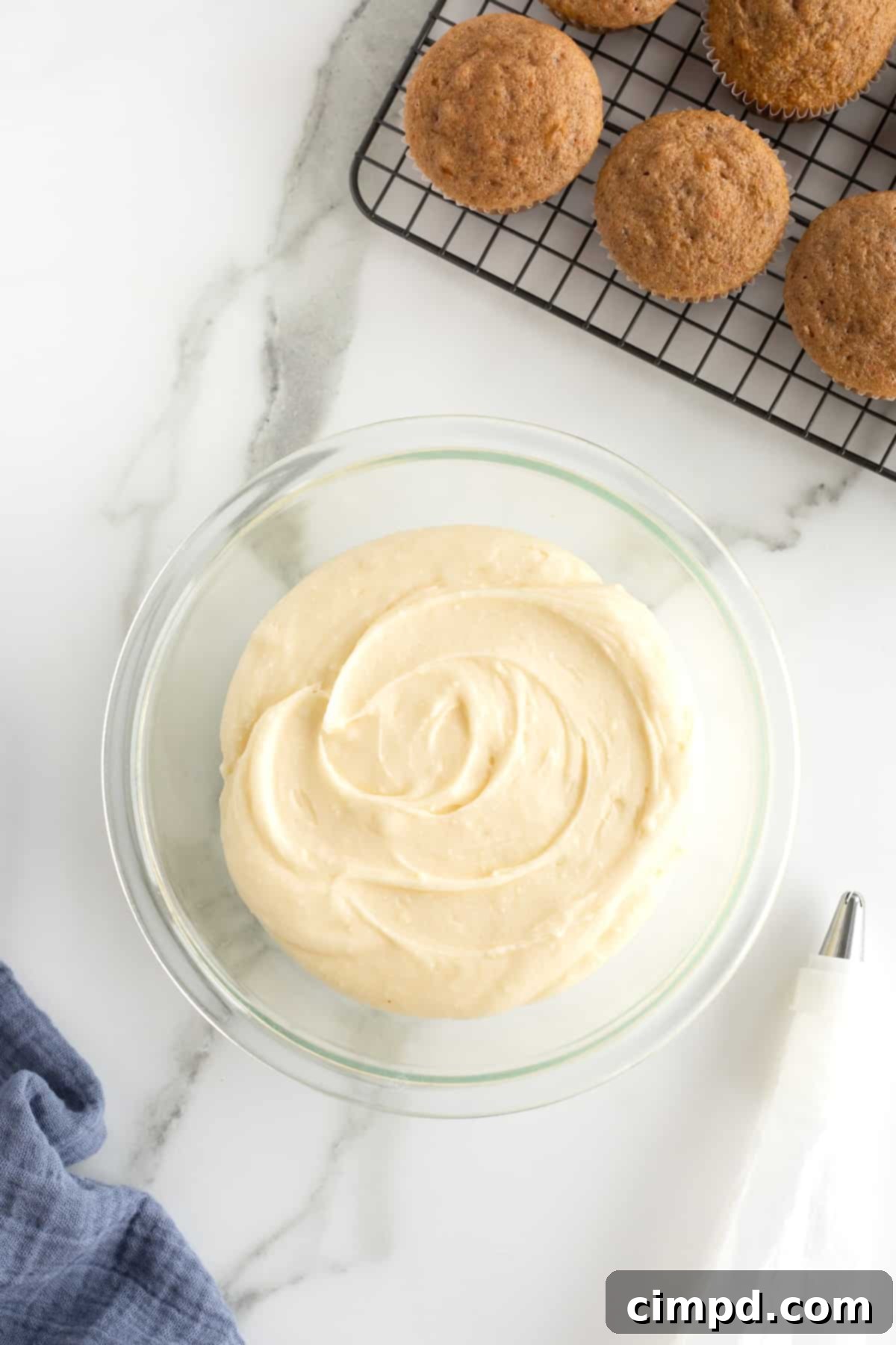 Whip Up Perfect Cream Cheese Frosting 8 A clear glass bowl of cream cheese icing sitting next to a cooling rack of cupcakes.