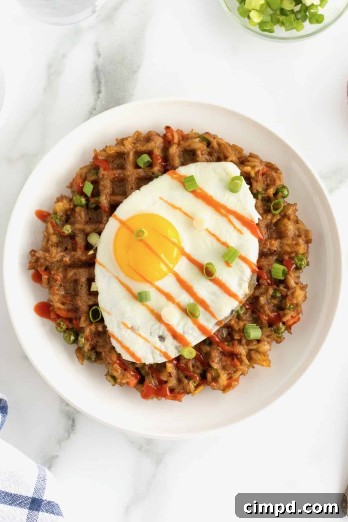 A sunny side up egg on top of a fried rice waffle on a white ceramic plate sprinkled with chopped green onions.