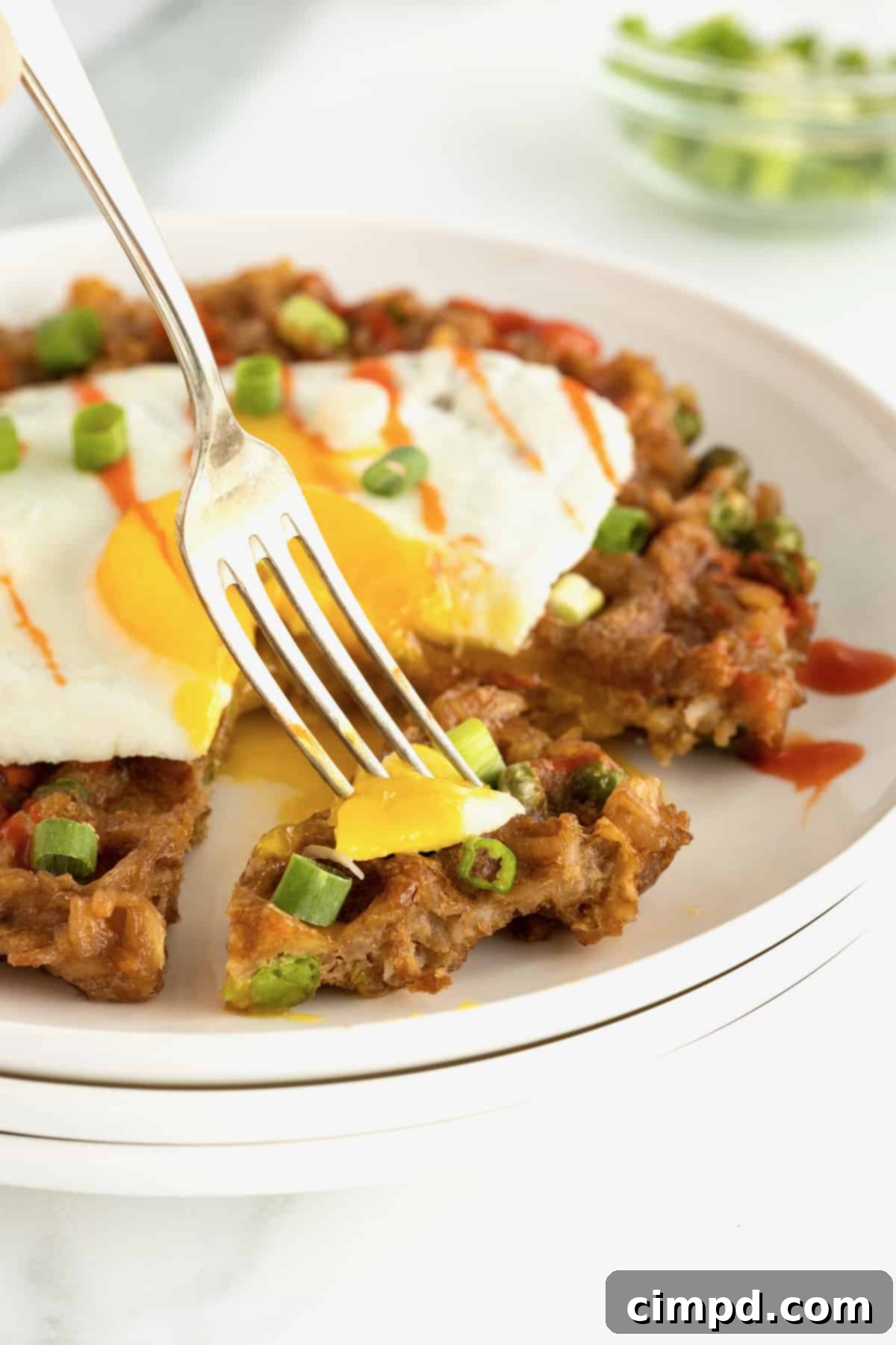 A fork with a bite of fried egg and leftover fried rice waffle, showcasing the crispy texture.