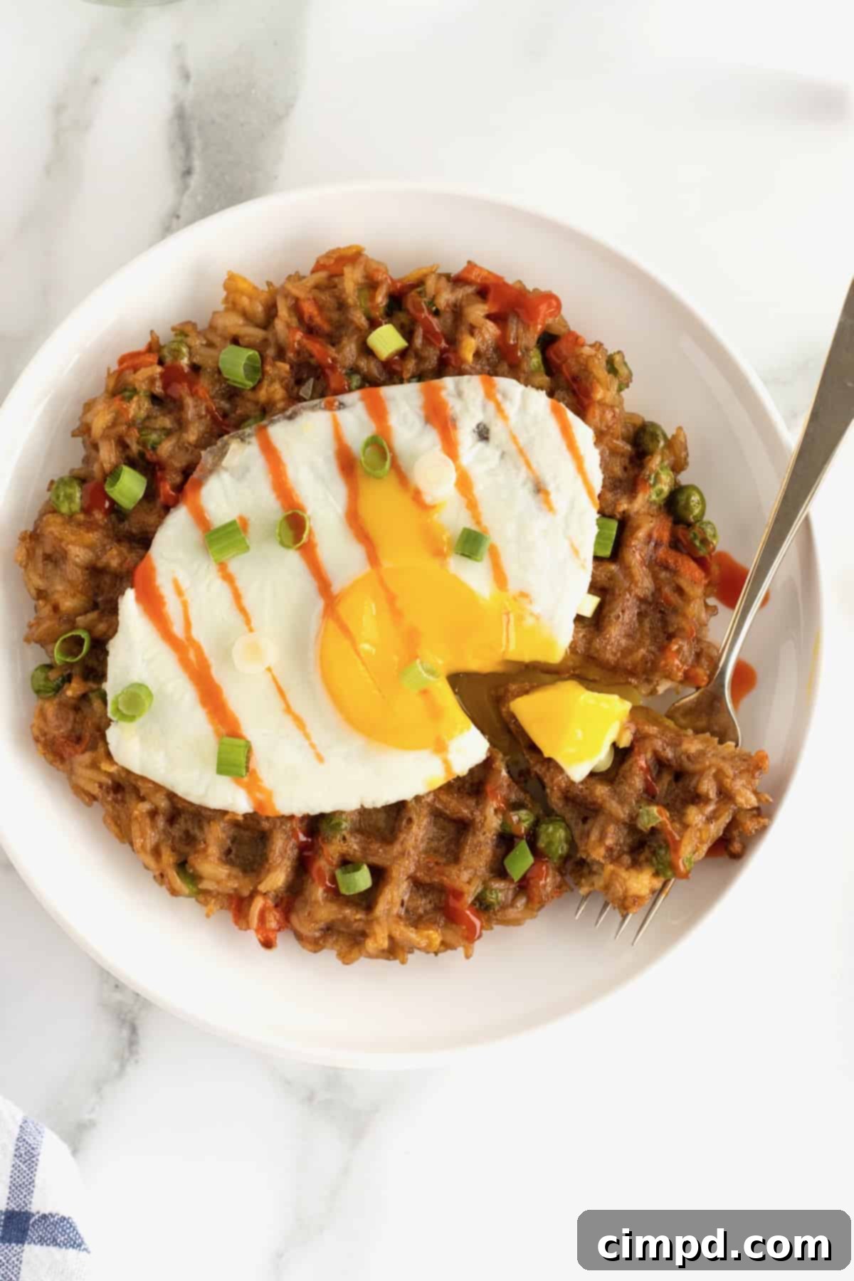A fork with a bite of fried egg and leftover fried rice waffle, ready to be enjoyed.
