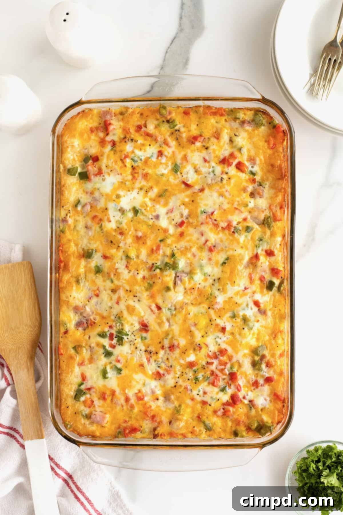 A fully cooked hash brown breakfast casserole in a glass dish, with a wooden spatula resting nearby, inviting you to serve.