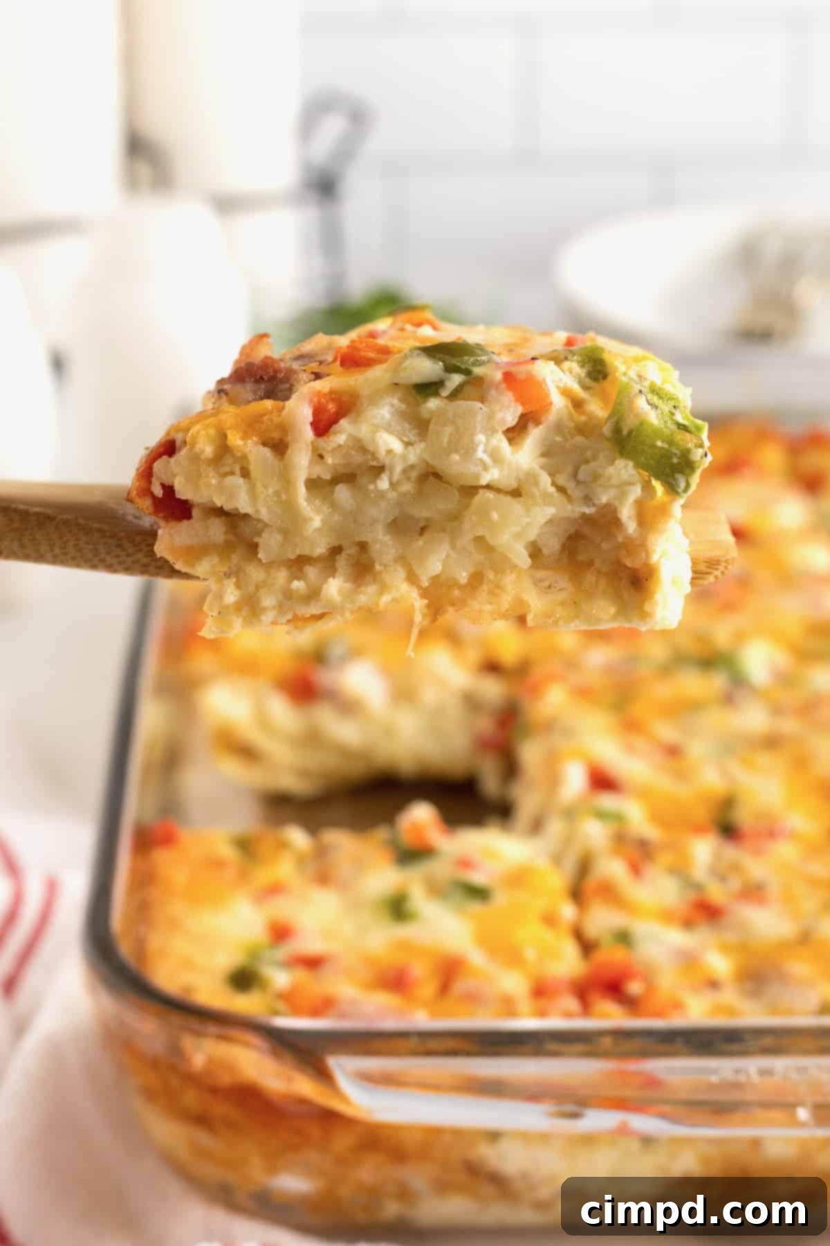 A perfectly portioned slice of breakfast casserole on a wooden spatula, with the full glass baking dish in the background, ready for serving.