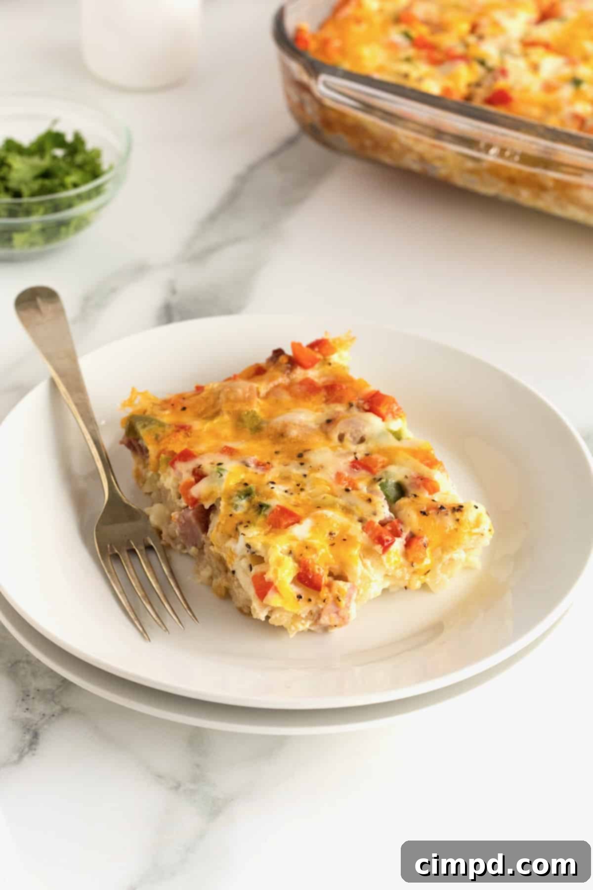 A single, delectable slice of hash brown casserole presented on a pristine white plate, accompanied by a fork.