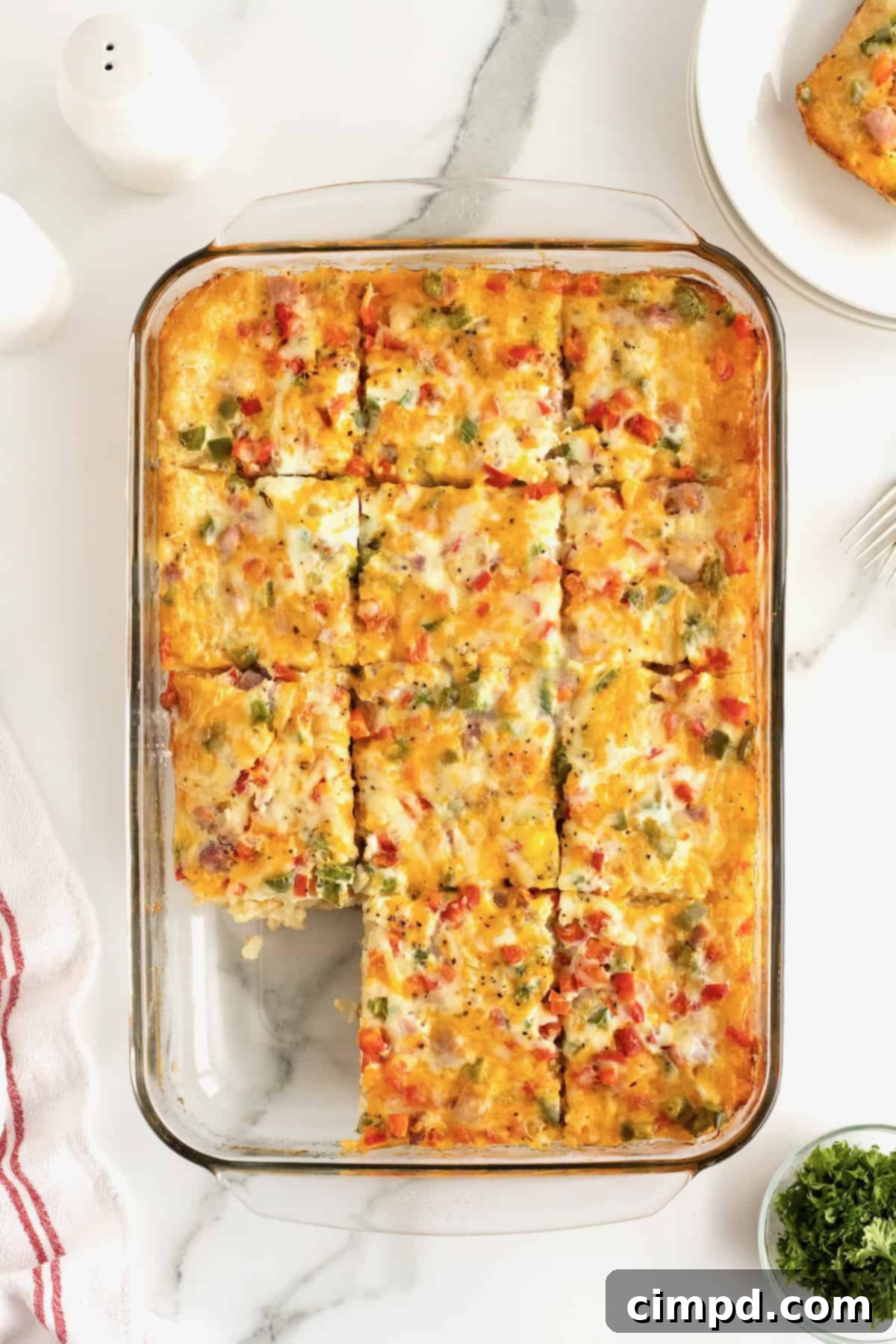 A golden-brown cooked breakfast casserole in a clear glass baking dish, with a slice already removed, revealing the delicious layers within.