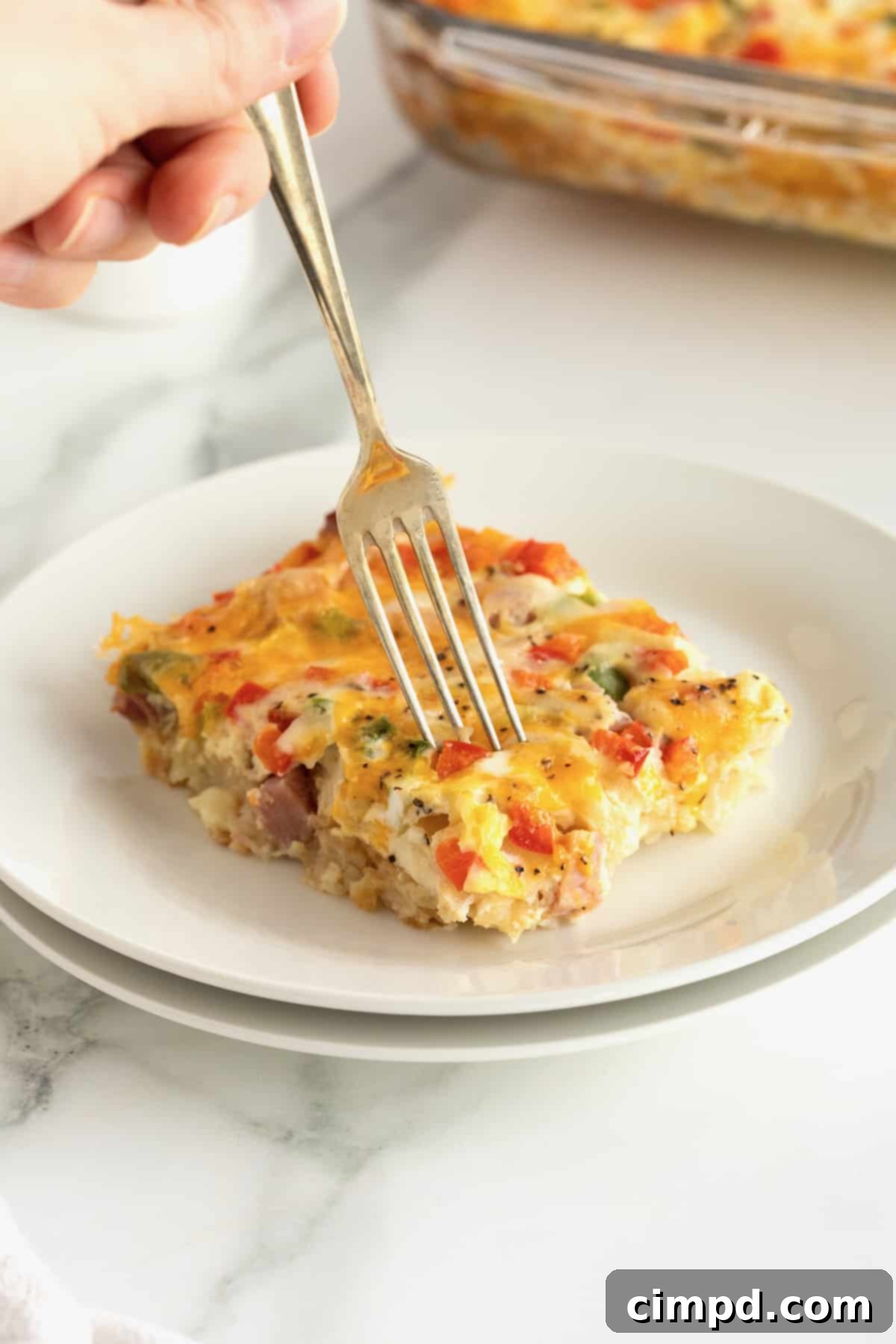 A close-up shot of a single slice of hash brown casserole on a white plate, highlighting its rich texture and cheesy topping.