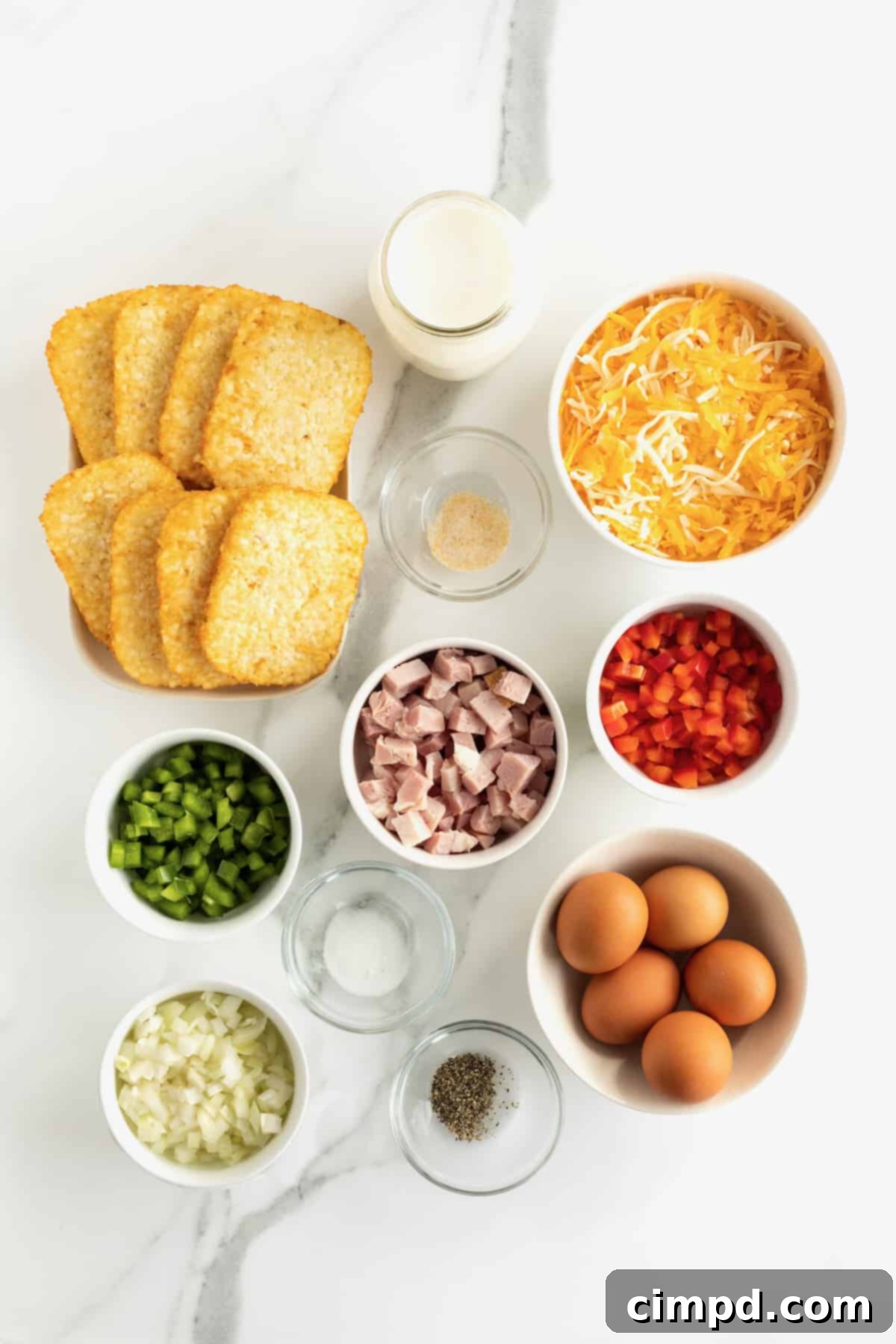 Ingredients for hash brown breakfast casserole meticulously arranged in small glass containers on a pristine marble counter, showcasing freshness and preparation.