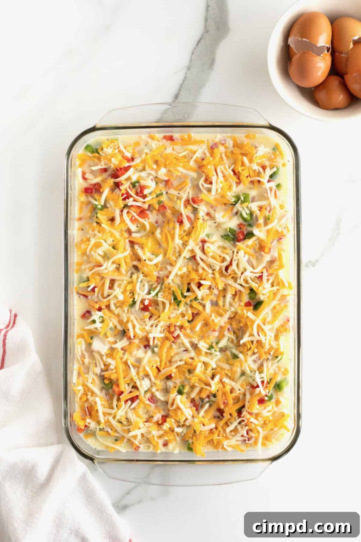 The step of carefully pouring the whisked egg mixture over the layered ingredients in the glass baking dish.