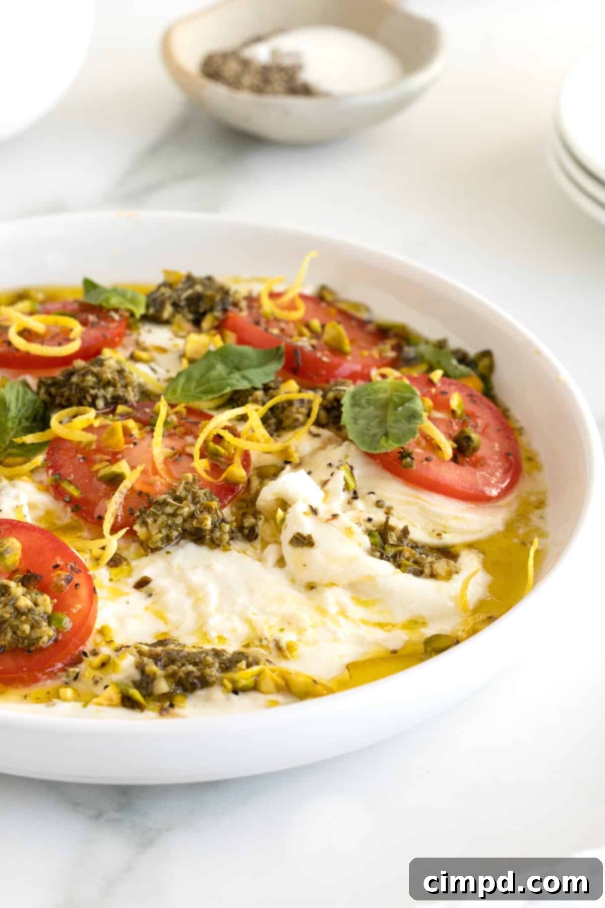 Velvet Burrata Caprese Board 11 A perfectly arranged Burrata Caprese platter on a round white dish, garnished with fresh basil, ready for serving with crostini.