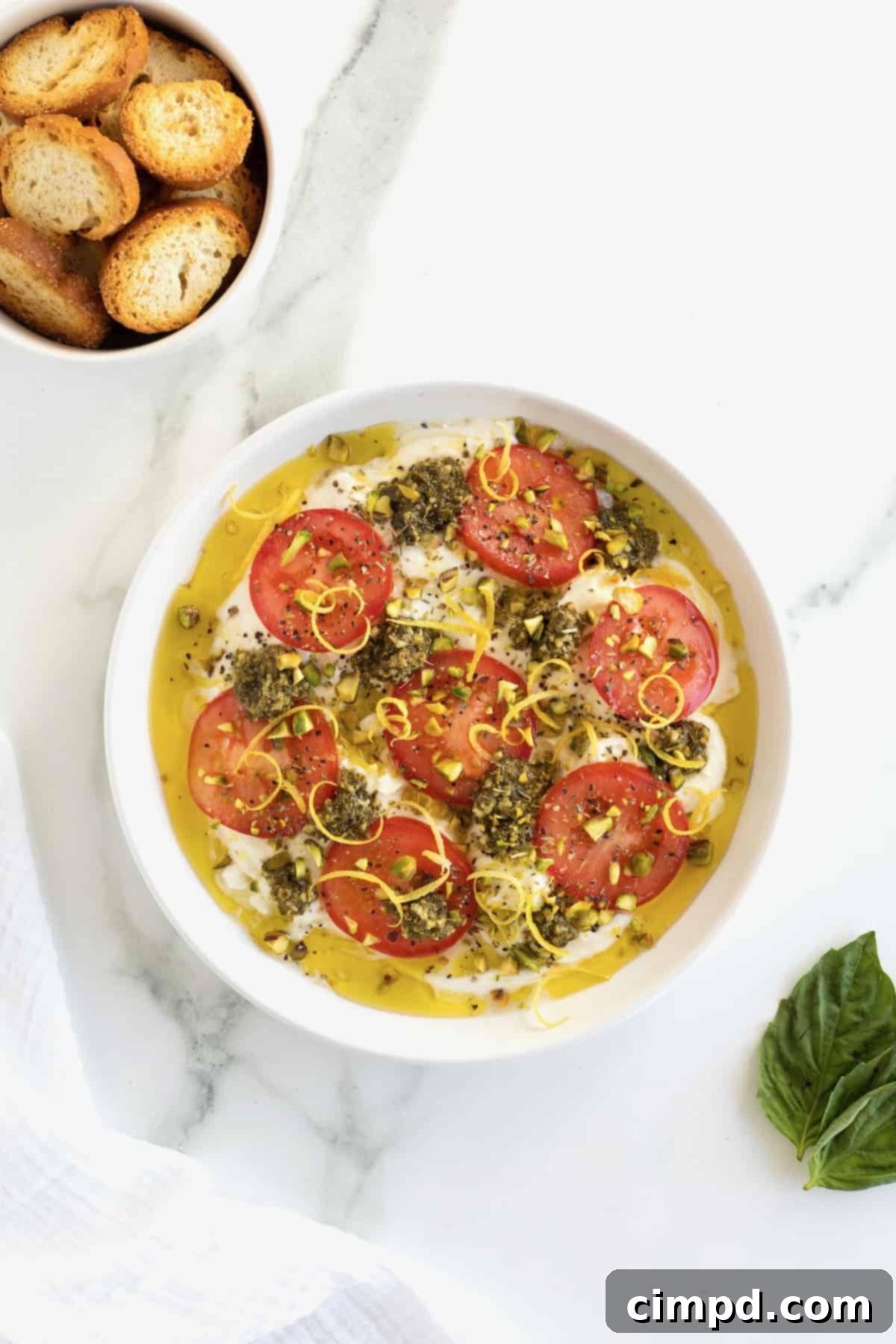 Velvet Burrata Caprese Board 9 A close-up image of the burrata caprese with pistachios, Italian seasoning, and lemon zest being sprinkled on top.