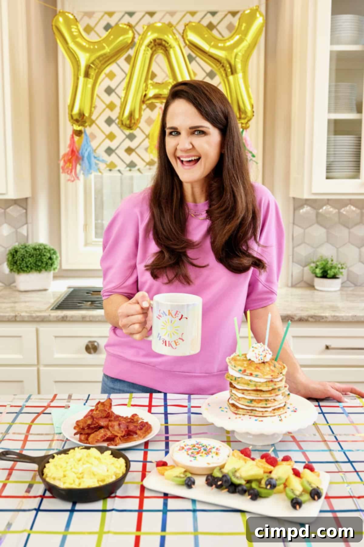 Ignite Your School Year 6 A delightful breakfast spread featuring fluffy soft scrambled eggs in a black cast iron skillet, crispy bacon on a white round plate, a towering stack of confetti pancakes on a white cake plate, and colorful fruit skewers with berries, oranges, pineapple, and blueberries on a rectangular white serving tray.