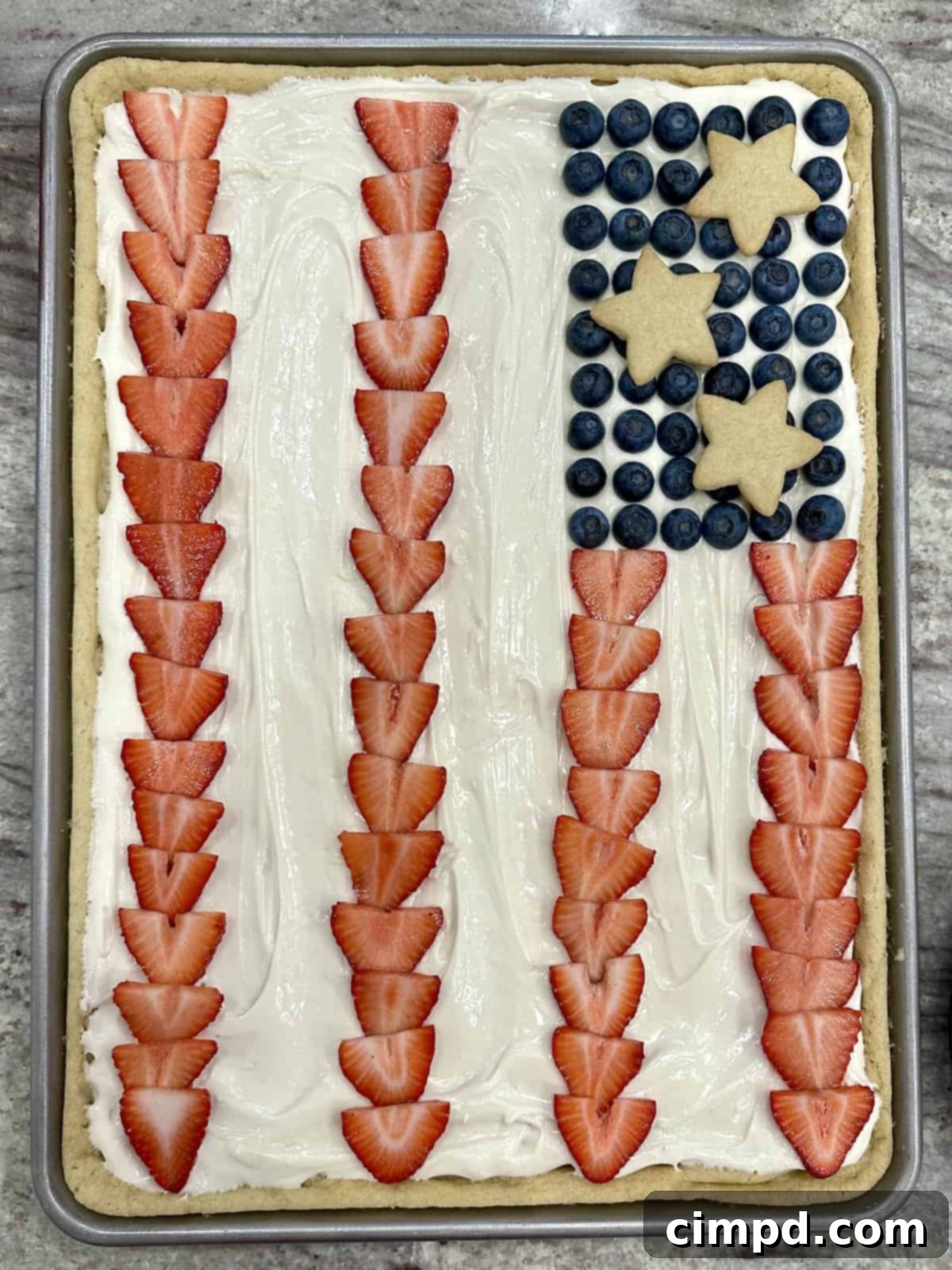 Star-Spangled Fruit Pizza with Cream Cheese Frosting 5 Close-up of the American Flag Fruit Pizza, showing the detailed arrangement of sliced strawberries, blueberries, and star cookies on the cream cheese frosting.
