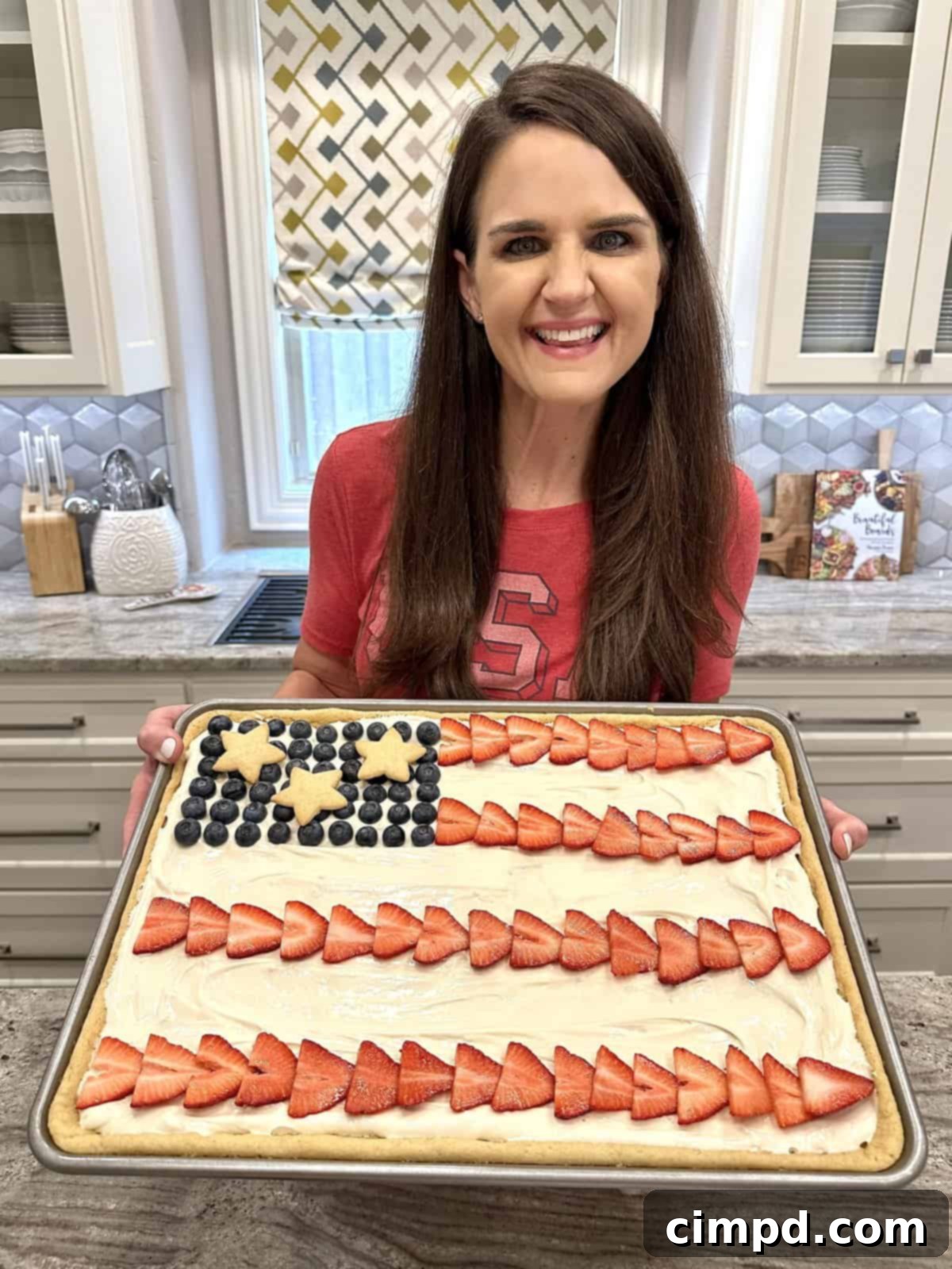 Star-Spangled Fruit Pizza with Cream Cheese Frosting 6 The BakerMama proudly holding a sheet pan of the finished American Flag Fruit Pizza, ready to be served.