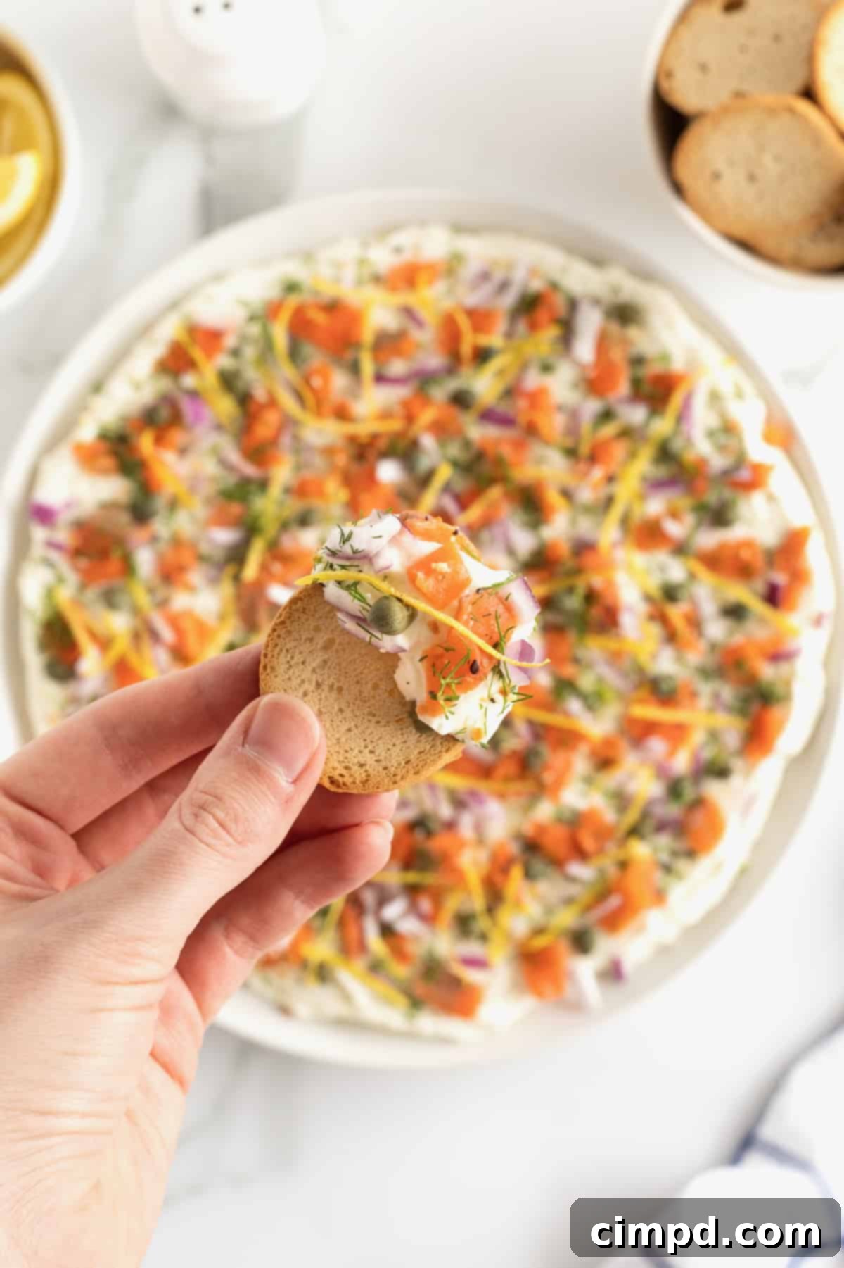 A round white serving platter showcasing a generous portion of smooth, creamy smoked salmon dip with bagel chips arranged neatly around it.