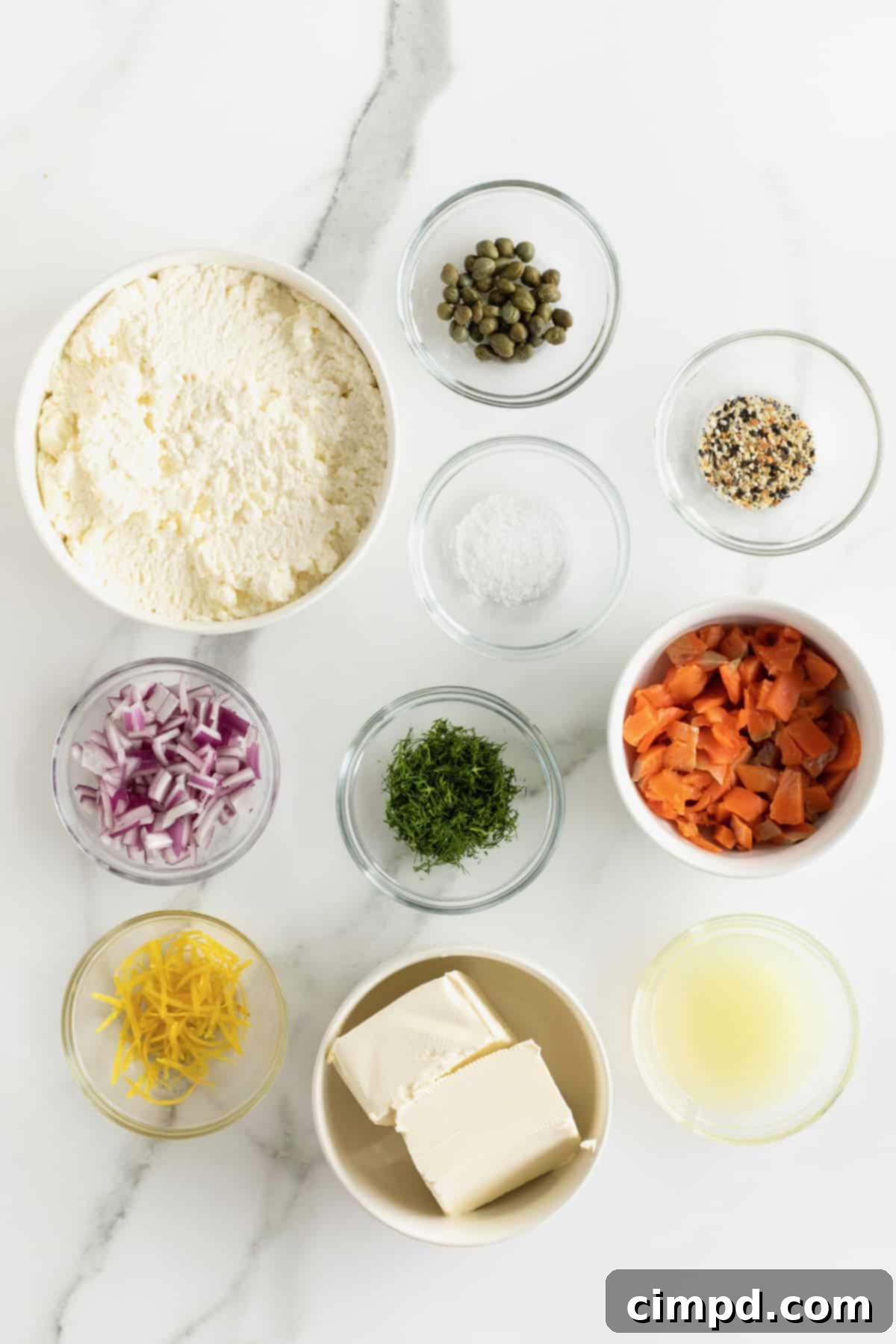 Individual glass dishes displaying the fresh ingredients for Smoked Salmon Bagel Dip: whole milk ricotta, cream cheese, chopped smoked salmon, capers, thinly sliced red onion, lemon zest, and fresh dill.