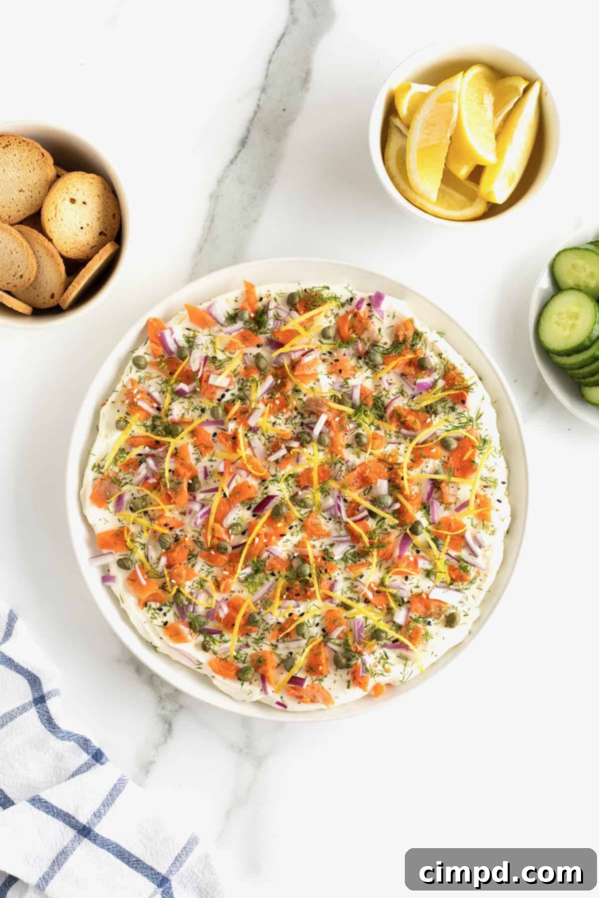 A beautifully arranged round white serving platter with the finished cream cheese smoked salmon dip, surrounded by an assortment of crispy bagel chips.