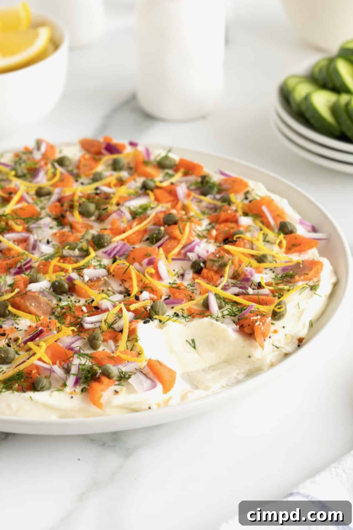 A close-up of the fresh toppings for the Smoked Salmon Bagel Dip, including sliced red onion, capers, lemon zest, everything bagel seasoning, and finely chopped fresh dill, all ready to be layered on the creamy base.