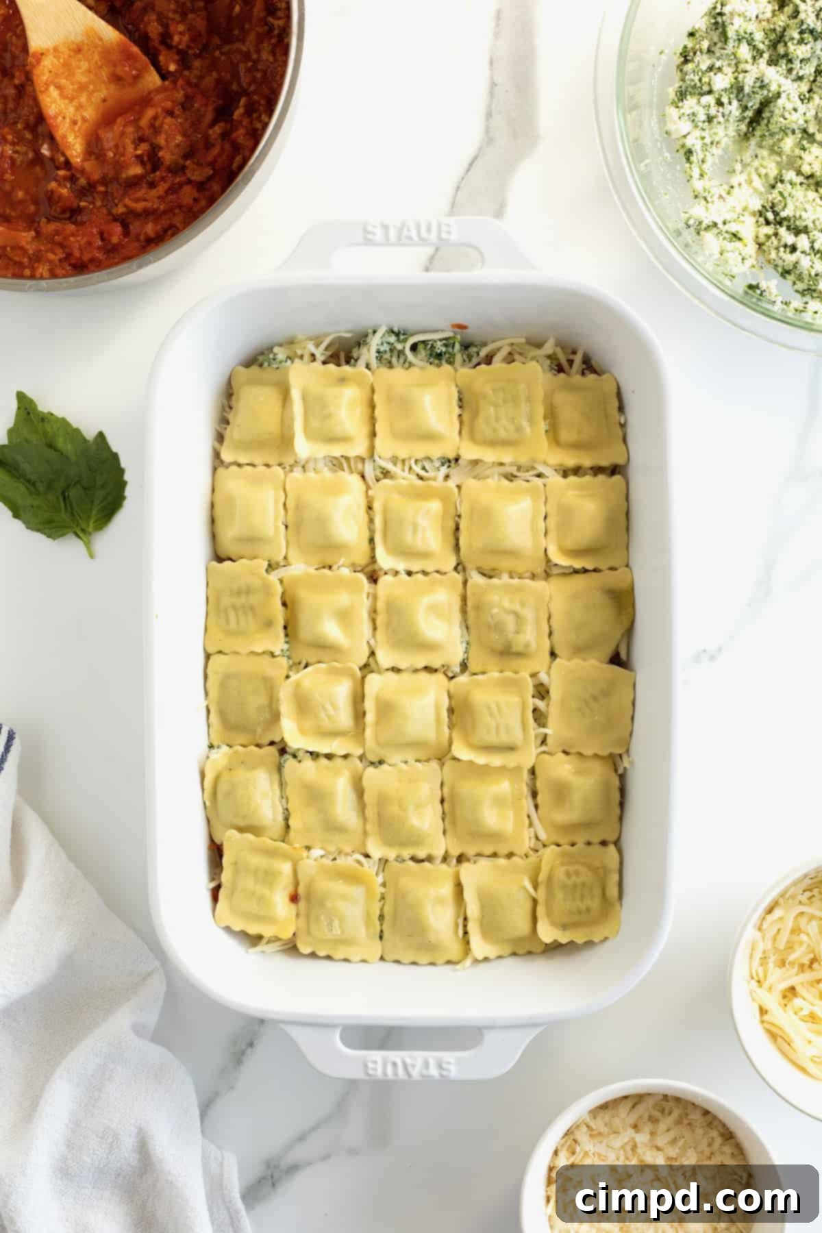 Ravioli placed in a single layer on top of shredded cheese in a white casserole dish.