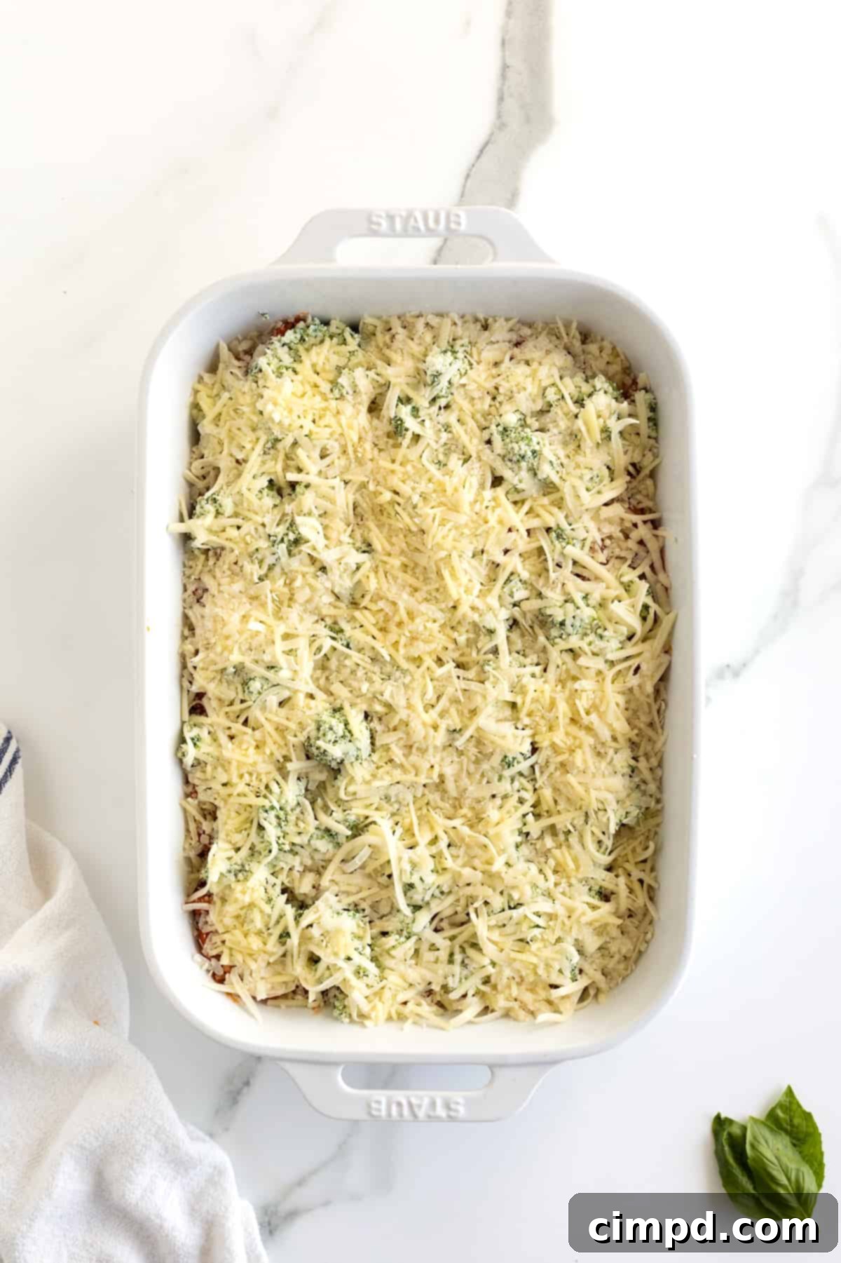 A white casserole dish of unbaked lasagna with shredded mozzarella and grated parmesan cheese on top.