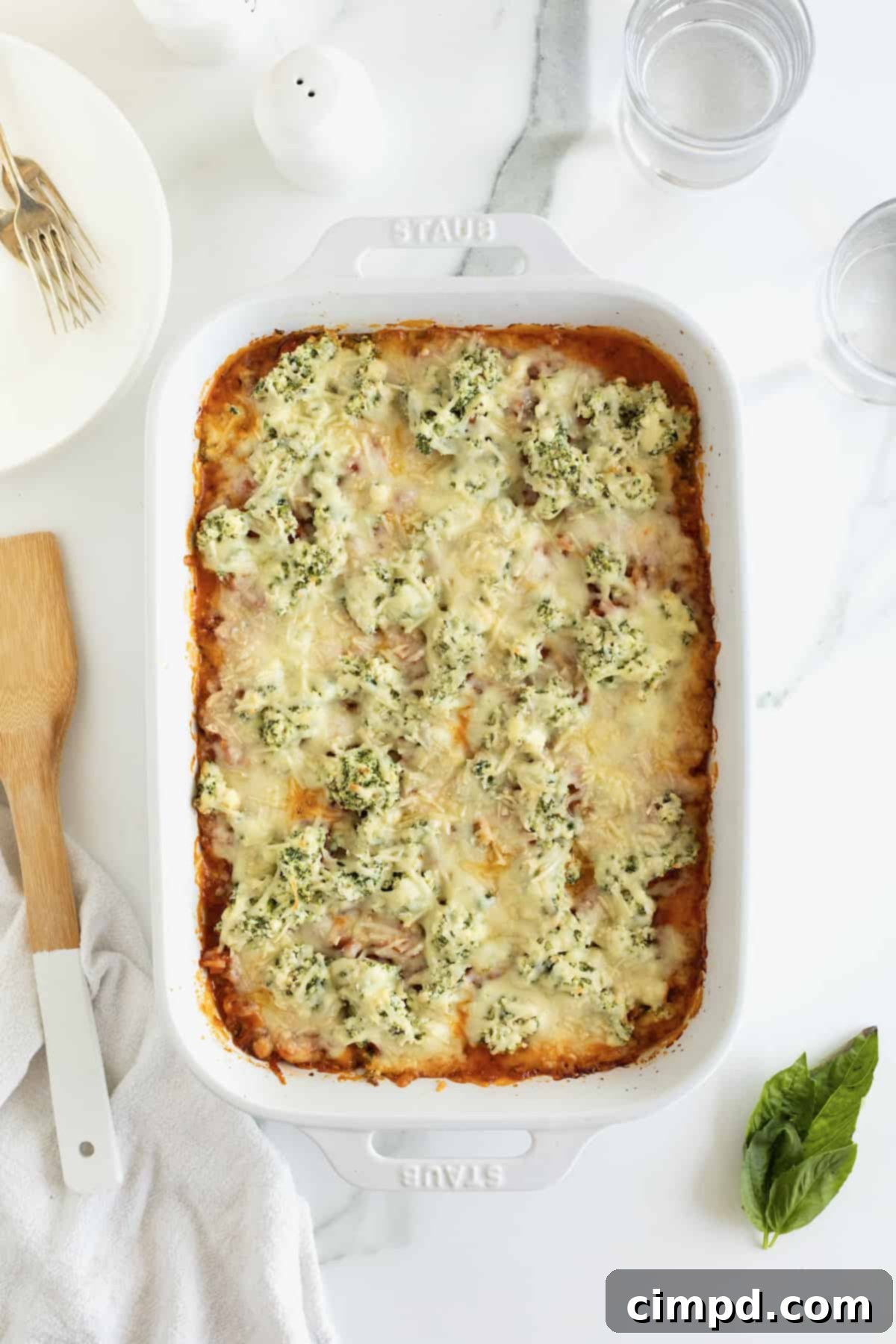 A white casserole dish with lasagna next to a wooden spoon.