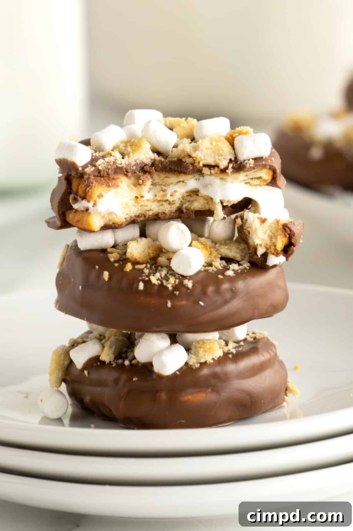 No-Bake Smores Cracker Bites 3 A close-up shot of a S'mores Cracker Bite with a small bite taken out, revealing the layers of crispy Ritz crackers, fluffy marshmallow creme, and a smooth chocolate candy coating, adorned with tiny marshmallow bits.