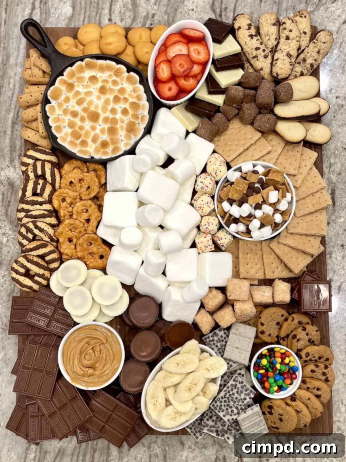 Your Guide to an Epic Smores Board 2 A large wooden board piled high with graham crackers, fluffy marshmallows, chocolate fudge stripe cookies, a warm skillet s'mores dip, fresh sliced strawberries and bananas, crispy pretzel chips, and classic chocolate chip cookies.