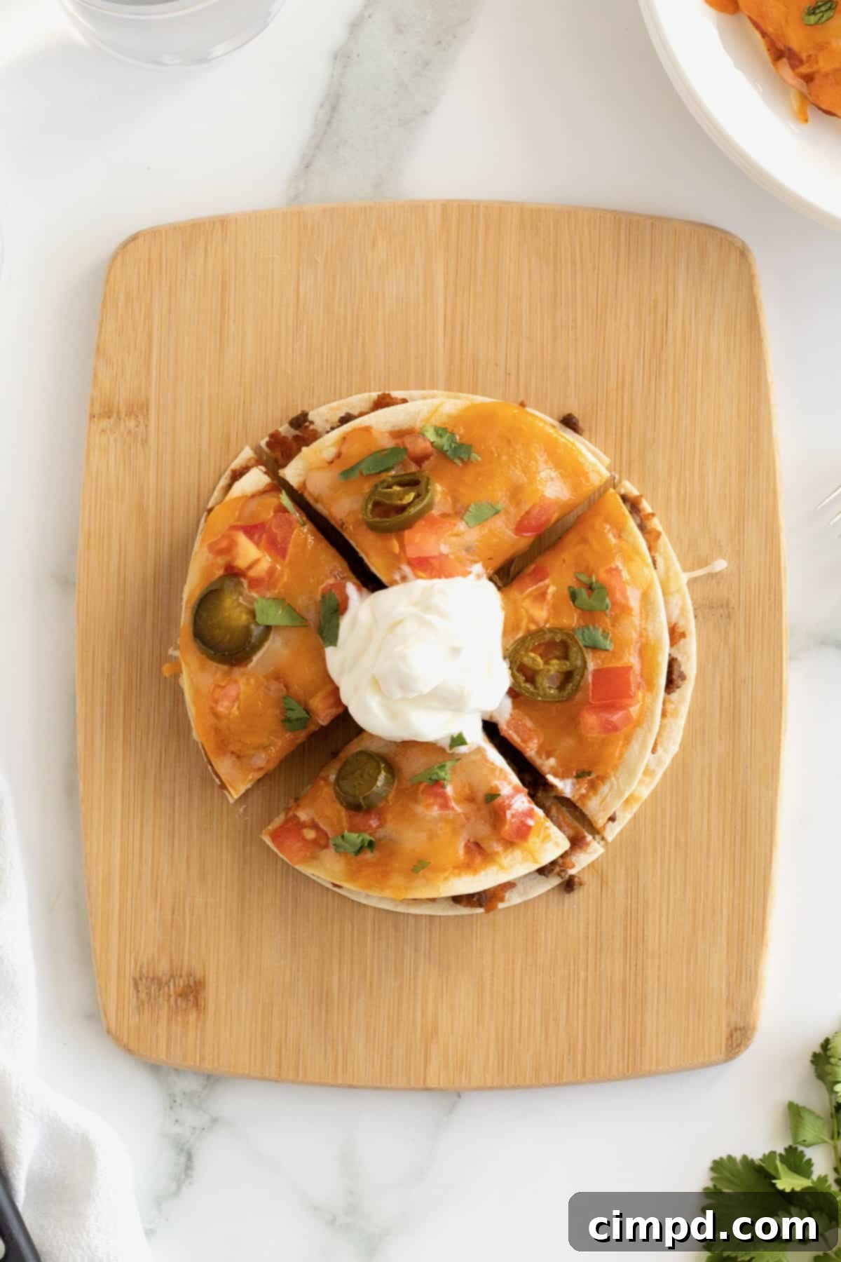 A homemade Taco Bell Mexican pizza cut in four slices on a wooden cutting board.