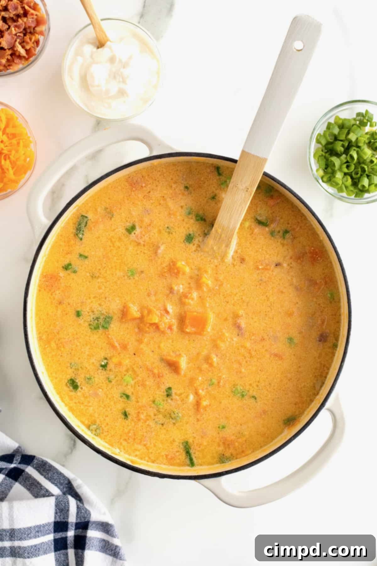 A white Dutch oven brimming with perfectly seasoned sweet potato soup, a wooden spoon resting inside, ready to be served.