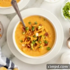 A white bowl of sweet potato soup on a white saucer with a spoon in it. The soup is topped with bacon bits, shredded yellow cheese and sliced green onion.