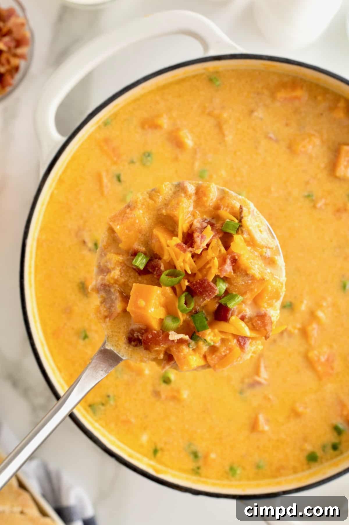 A ladle filled with creamy baked sweet potato soup, perfectly positioned above a pristine white Dutch oven brimming with the golden-hued soup.