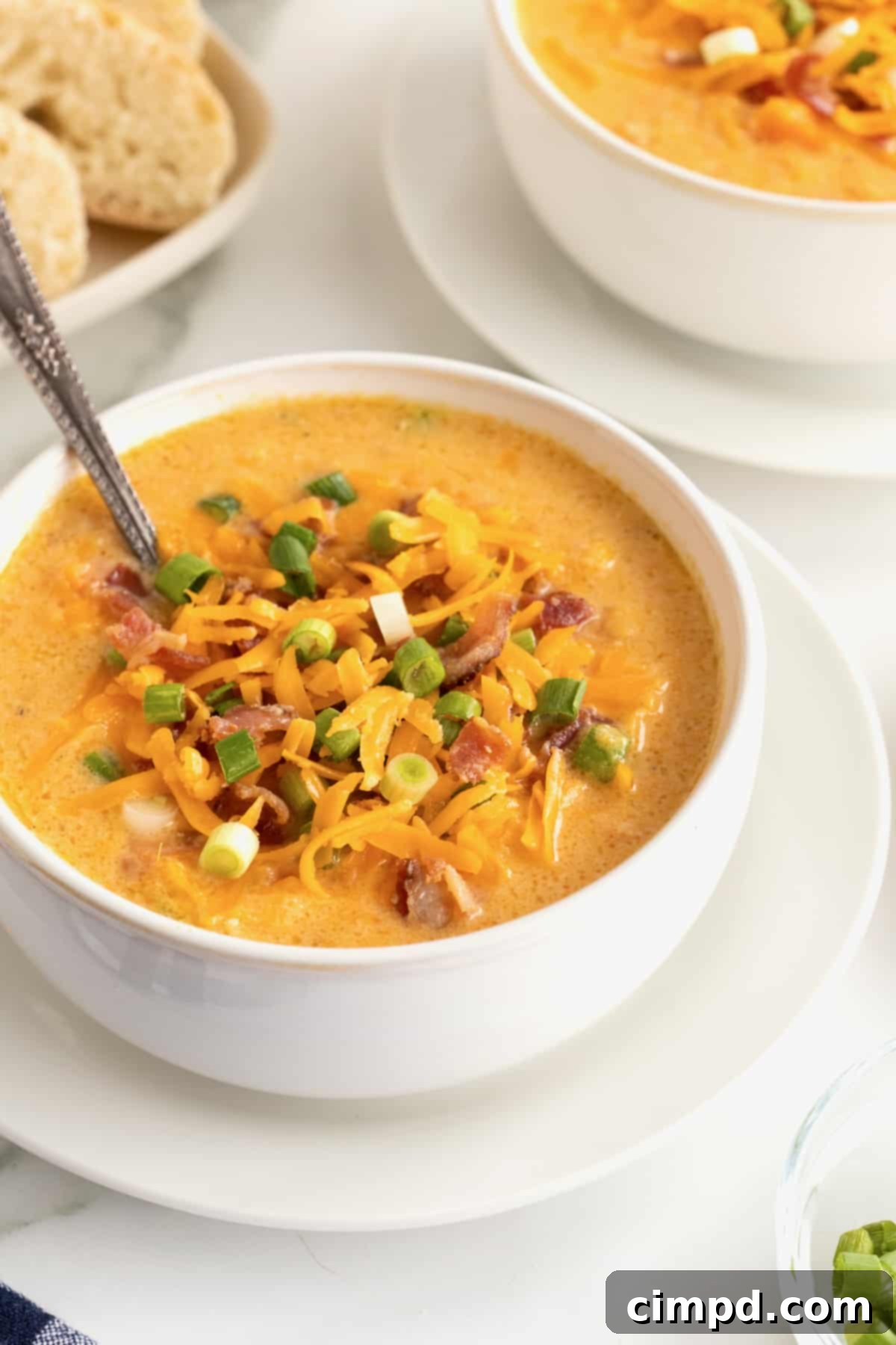 A white bowl of comforting sweet potato soup, topped with crunchy bacon bits, vibrant shredded yellow cheese, and fresh sliced green onions, with a spoon nestled in the bowl.