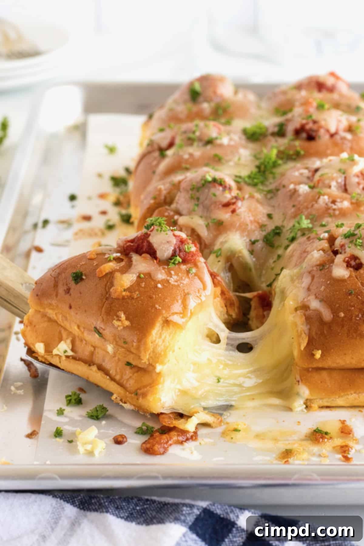 Close-up of golden brown Meatball Stuffed Garlic Rolls with bubbling cheese and a hint of fresh herbs on a baking sheet.