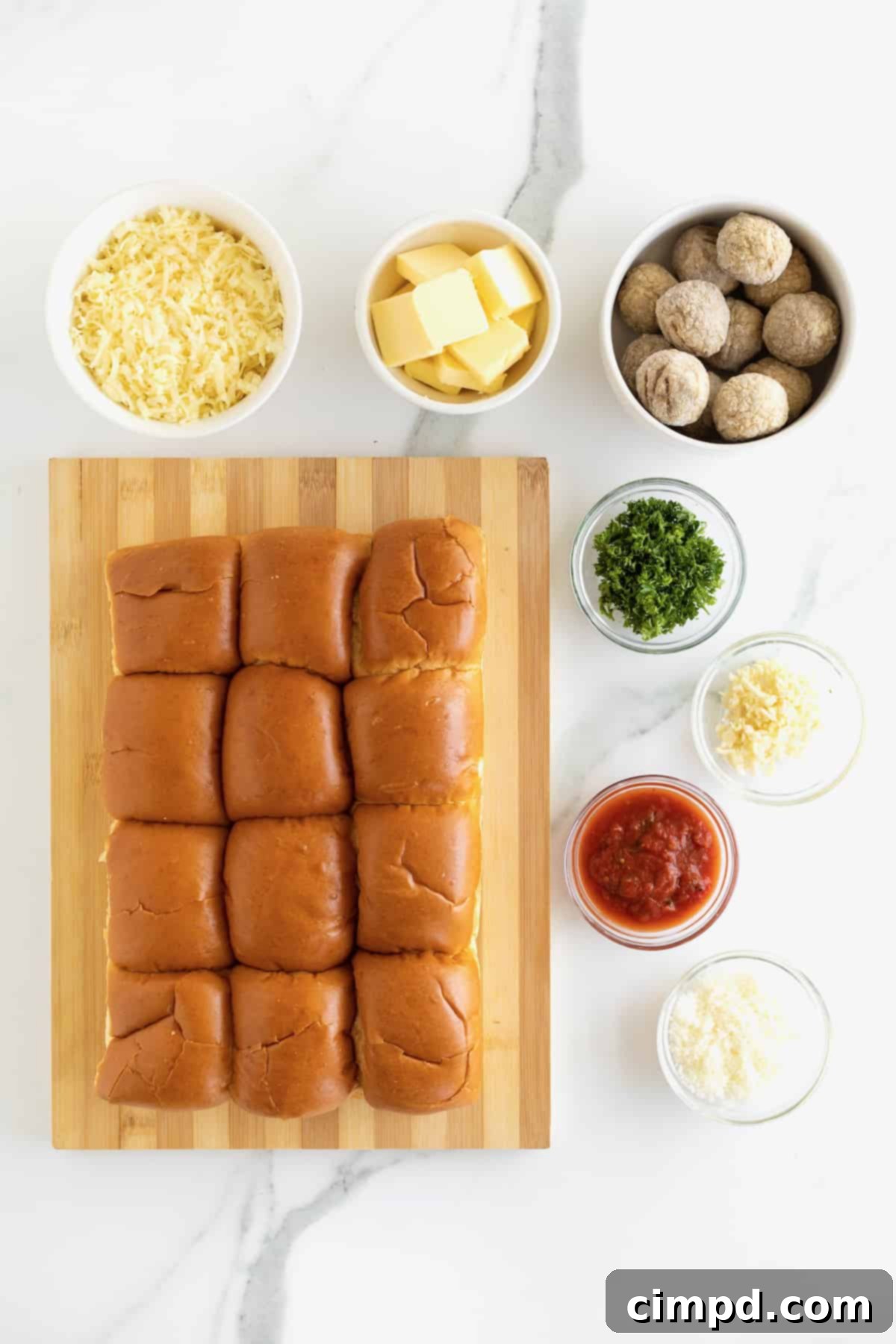 A flat lay of all the essential ingredients for Meatball Stuffed Garlic Rolls: savory rolls, unsalted butter, minced garlic, grated Parmesan, fresh parsley, marinara sauce, frozen meatballs, and shredded mozzarella cheese.