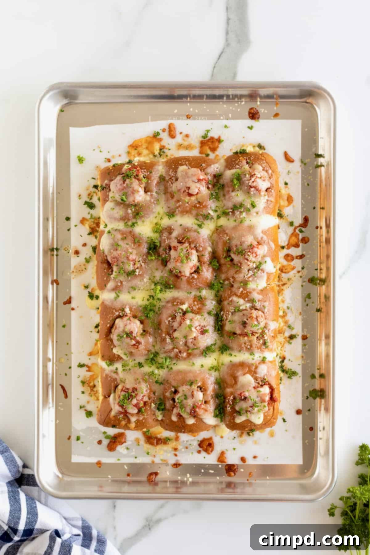 A baking sheet filled with perfectly golden and cheesy Meatball Stuffed Garlic Rolls, fresh out of the oven, sprinkled with fresh parsley.