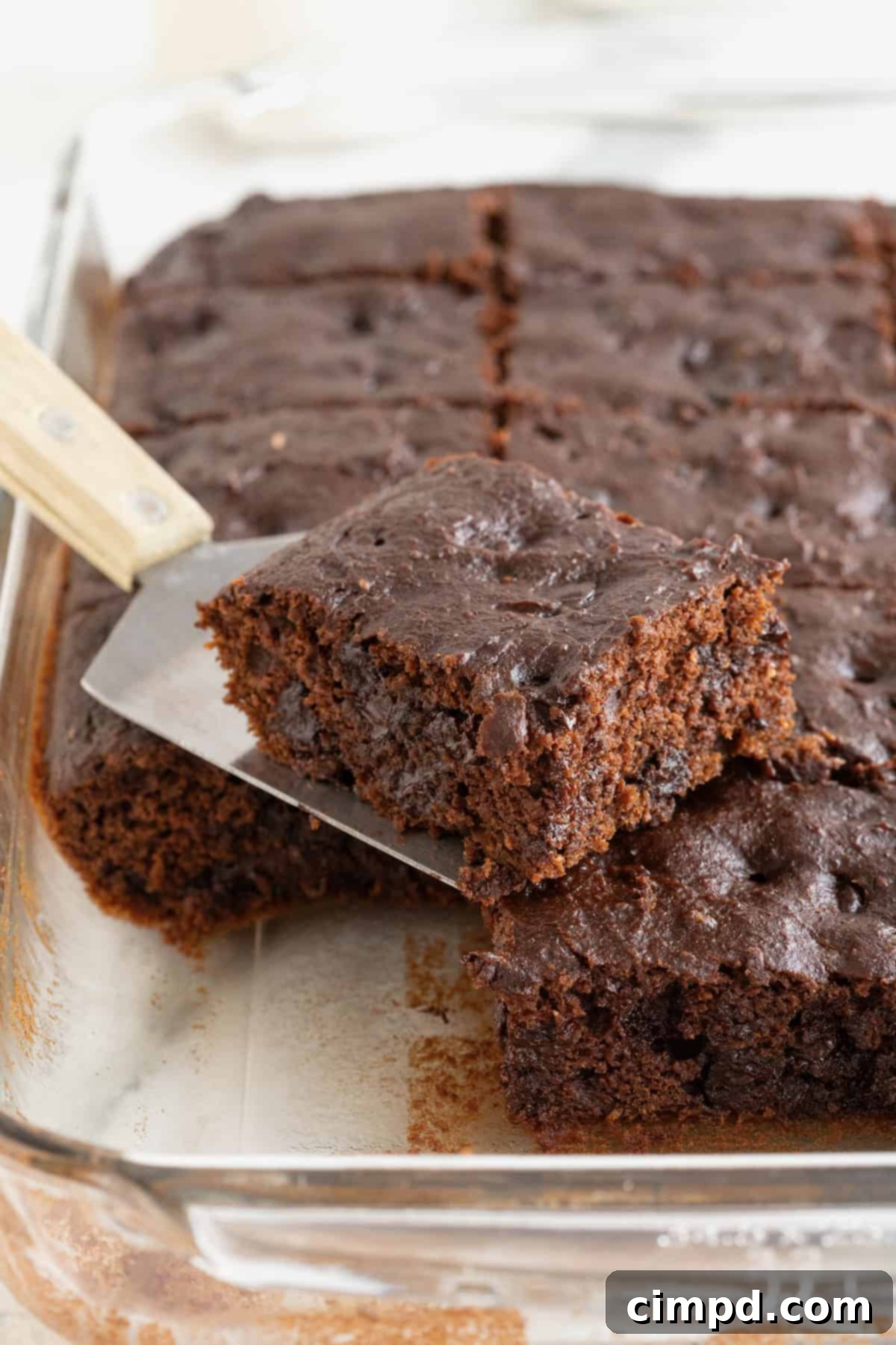 Warm pumpkin brownies cooling in a glass baking dish, with a spatula lifting one perfect square out, highlighting its moist interior.
