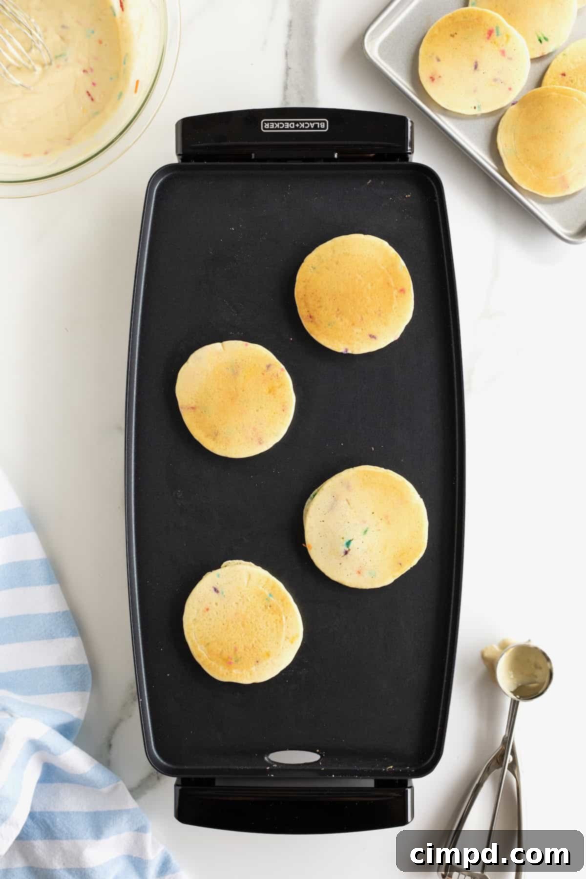 Pancakes with rainbow sprinkles in them on the griddle.