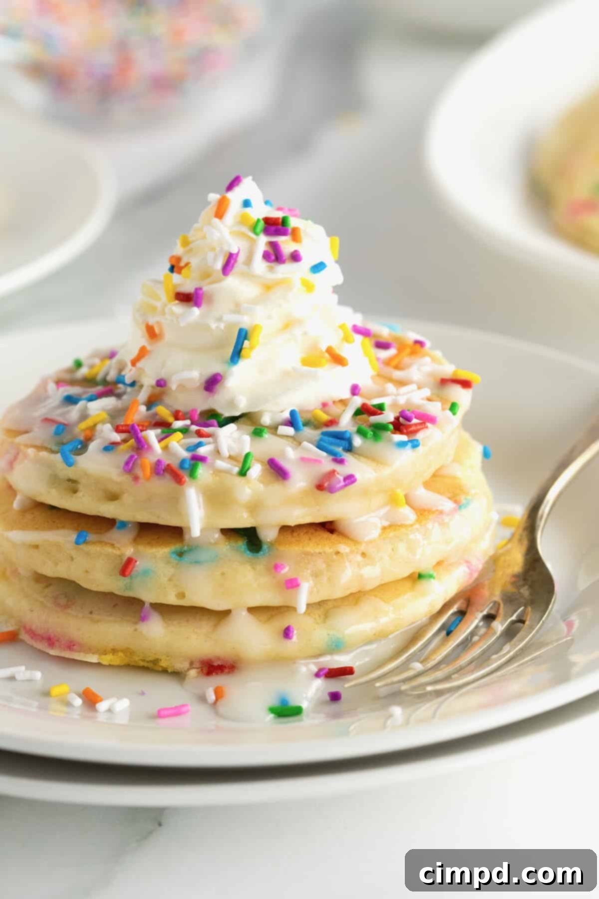 Fluffy pancakes with colorful confetti sprinkles, topped with whipped cream and more sprinkles.