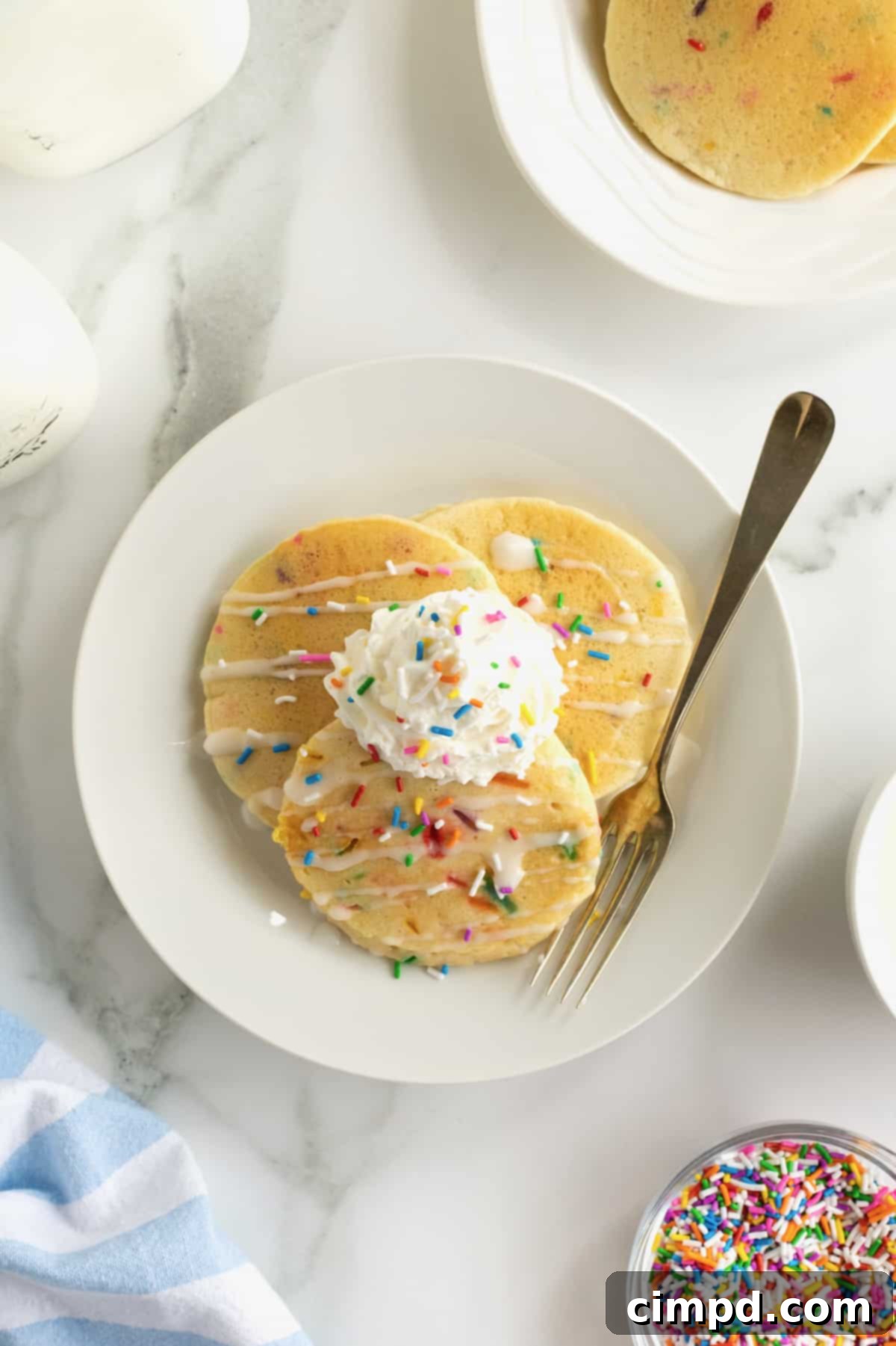 Fluffy pancakes with colorful confetti sprinkles, topped with whipped cream and more sprinkles.
