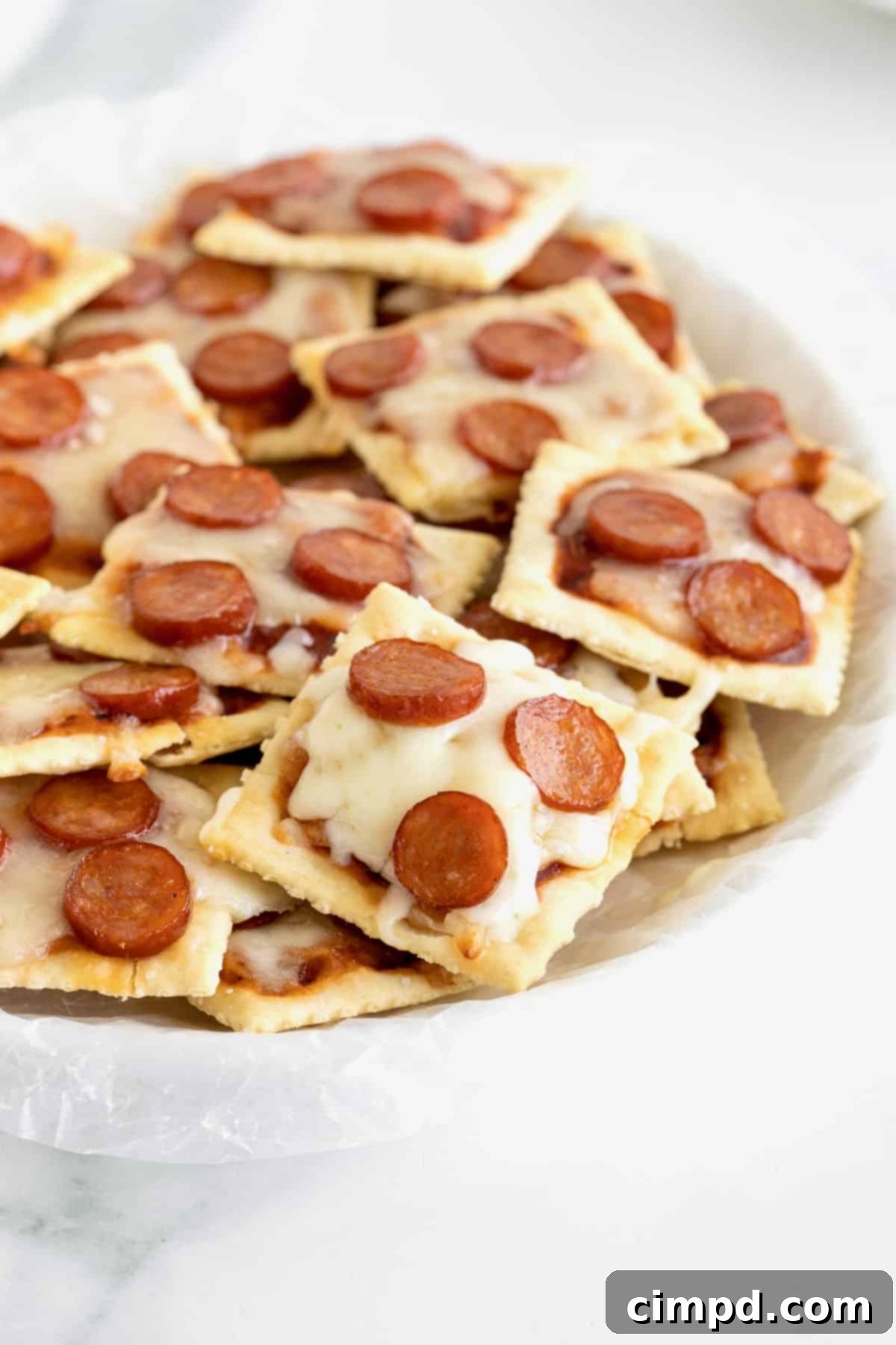 Crispy Pizza Bites 4 A hand reaching for a pizza bite made with saltine crackers, melted mozzarella, and mini pepperoni on a baking sheet.