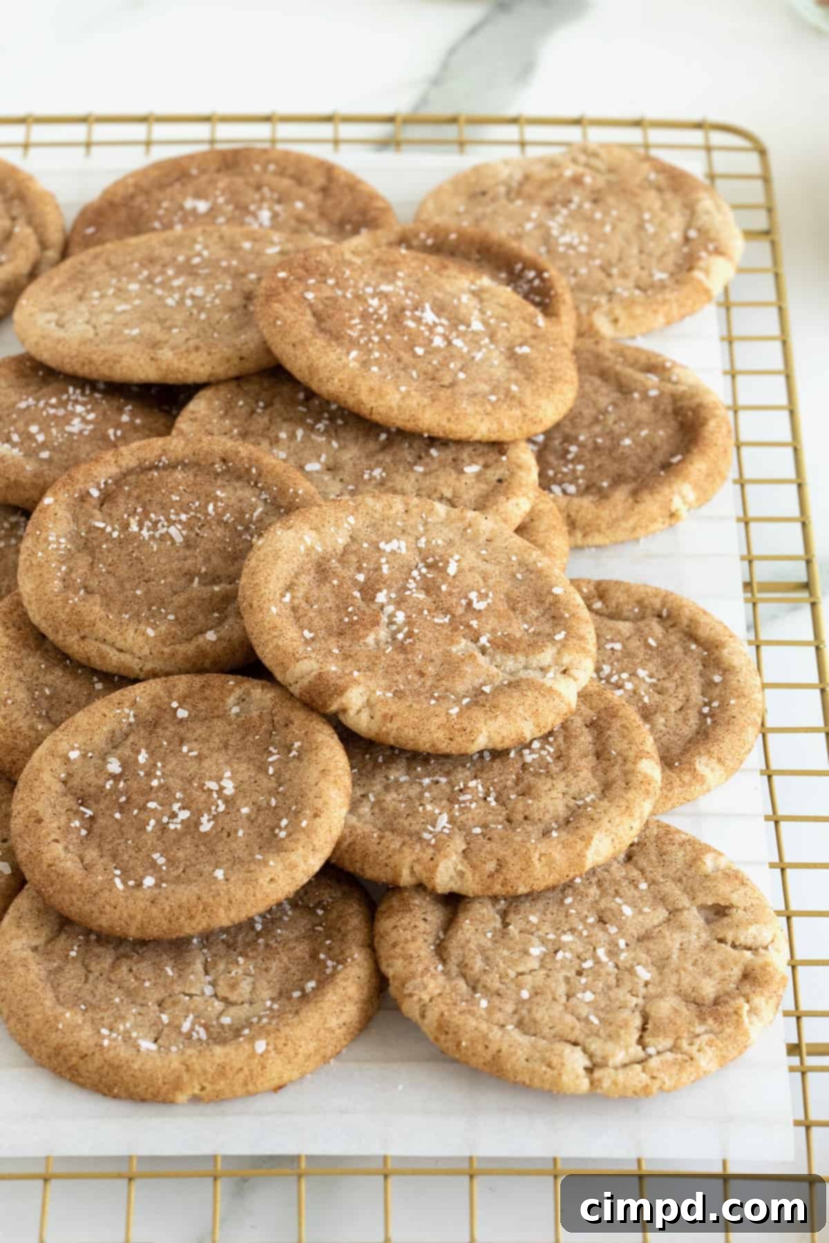 Snickerdoodle cookies sprinkled with sea salt piled on a parchment lined cooling rack. 