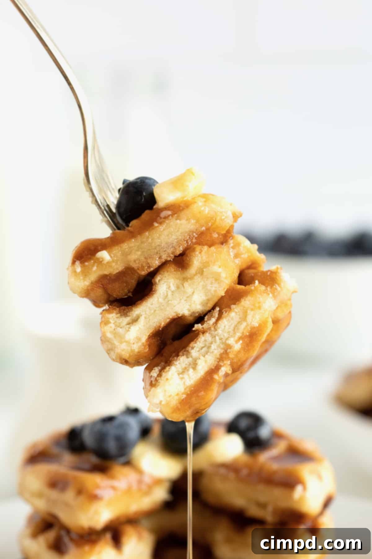 Glazed Waffle Rings 4 A bite of three donut waffles stacked together with fresh blueberries and maple syrup, showcasing the soft interior.