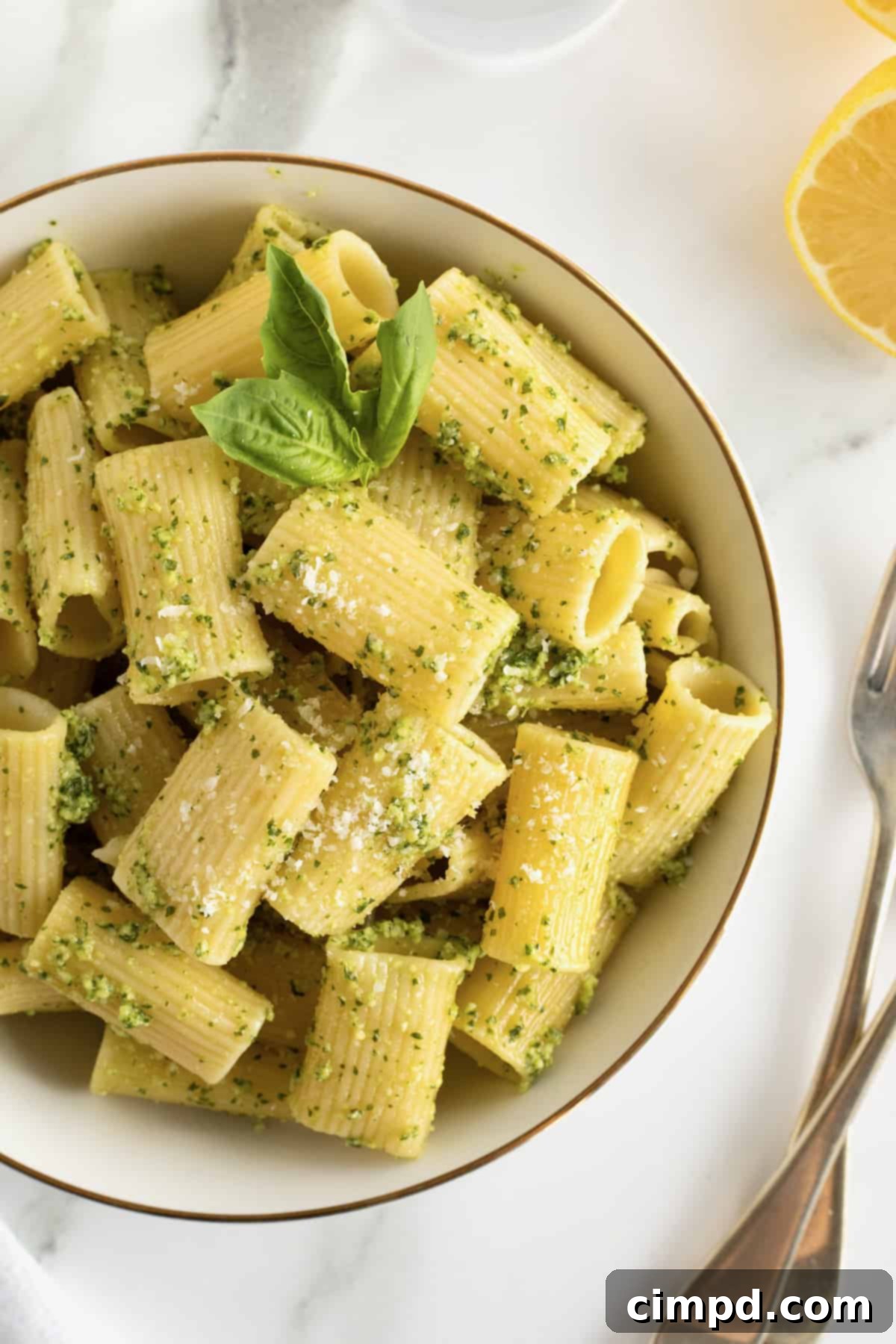 Crafting Your Own Fresh Basil Pesto 4 A large white serving dish showcasing pasta generously coated in pesto, adorned with a sprig of fresh basil.