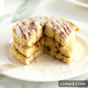 Cinnamon Swirl Pancakes 10 A stack of three pancakes made out of canned cinnamon rolls drizzled with icing on a white plate.