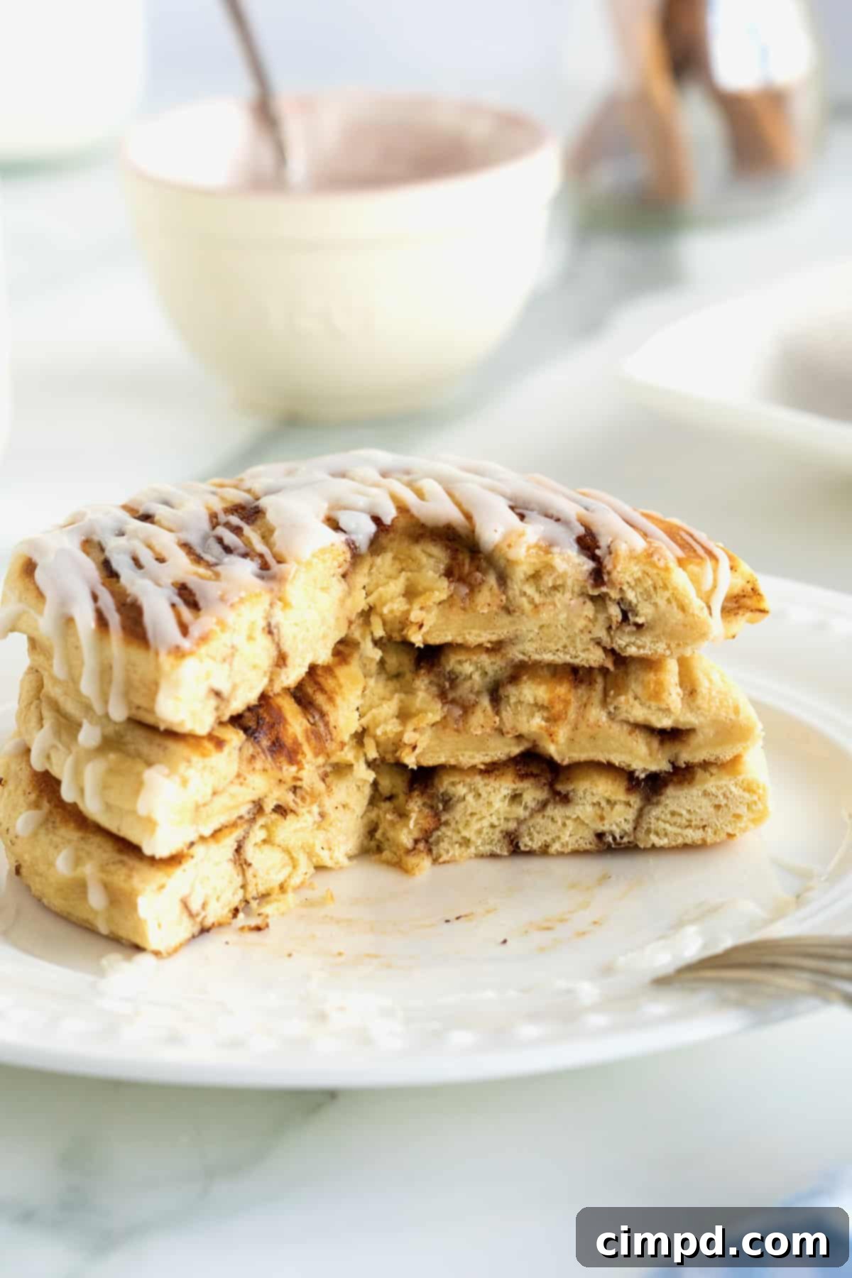 Cinnamon Swirl Pancakes 5 A stack of three pancakes made out of canned cinnamon rolls on a white plate drizzled with icing.
