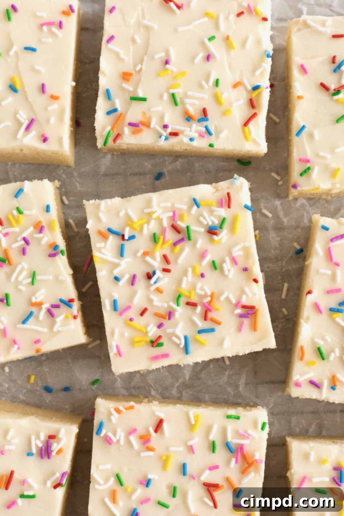 Soft Frosted Sugar Cookie Bars 5 A square sugar cookie bar with white cream cheese icing and rainbow sprinkles on a sheet pan.