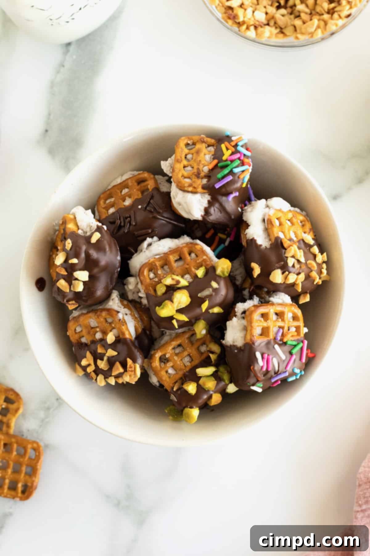A white serving bowl filled with pretzel ice cream sandwich bites dipped in chocolate and coated in sprinkles.